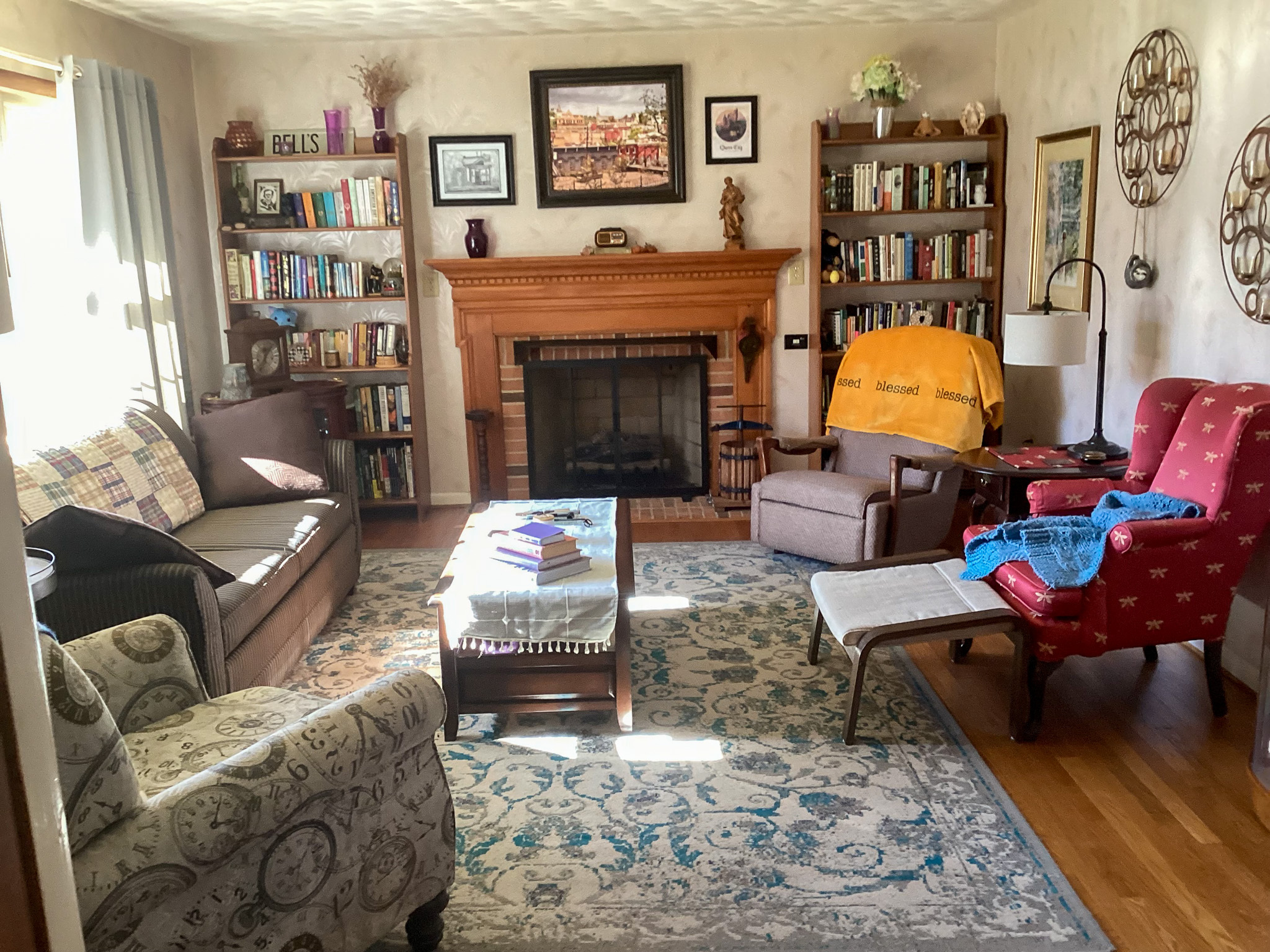Cozy living room with a fireplace, two bookcases, multiple chairs and sofas, a patterned rug, and warm natural light from a window on the left inside the home of Sponsored Residential Providers Bill and Heather Terry in Staunton, Virginia.