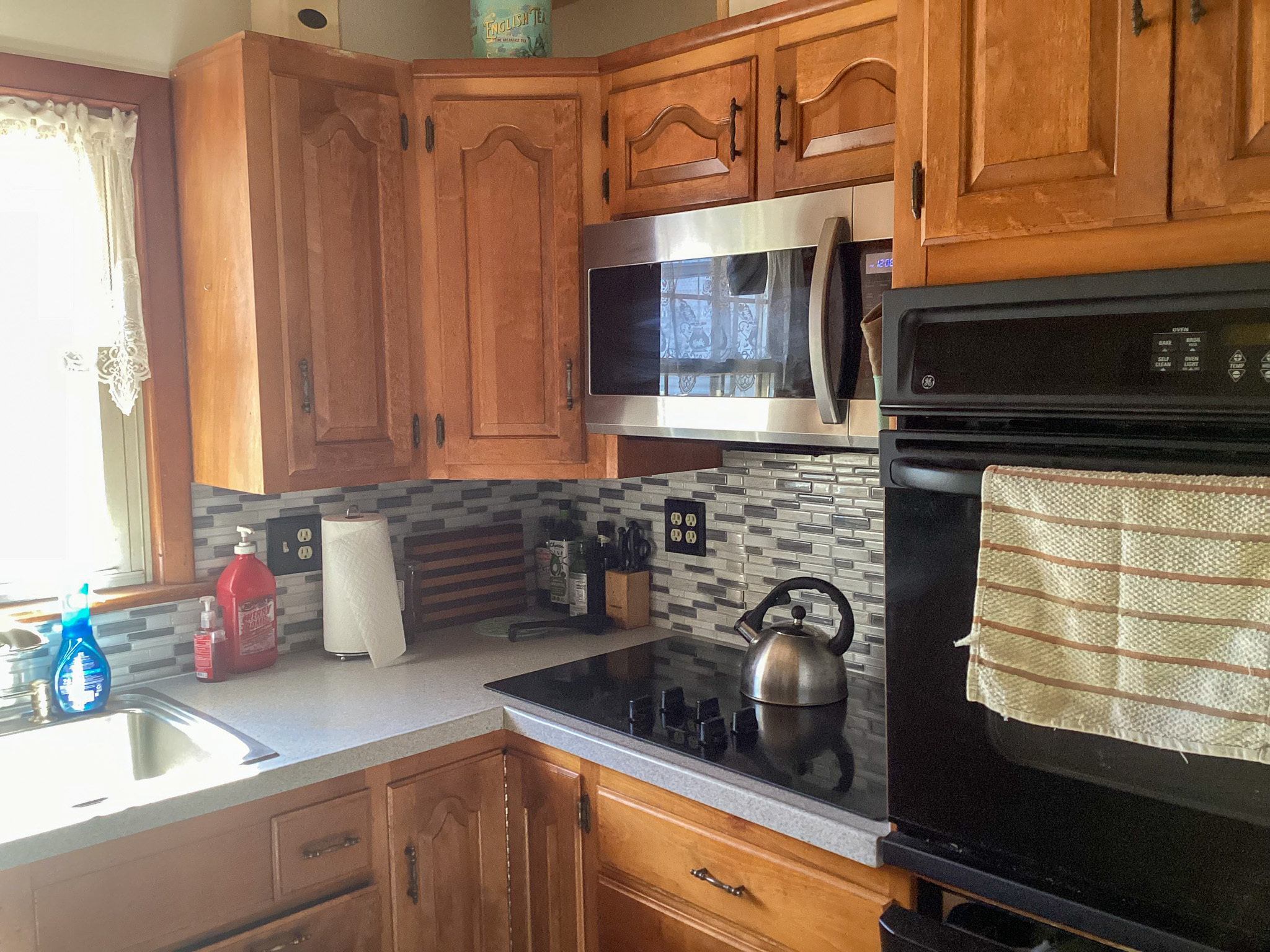 Kitchen with wood cabinets, stainless steel microwave, electric cooktop with kettle, built‑in oven, tiled backsplash, and a sink by a window inside the home of Sponsored Residential Providers Bill and Heather Terry in Staunton, Virginia.