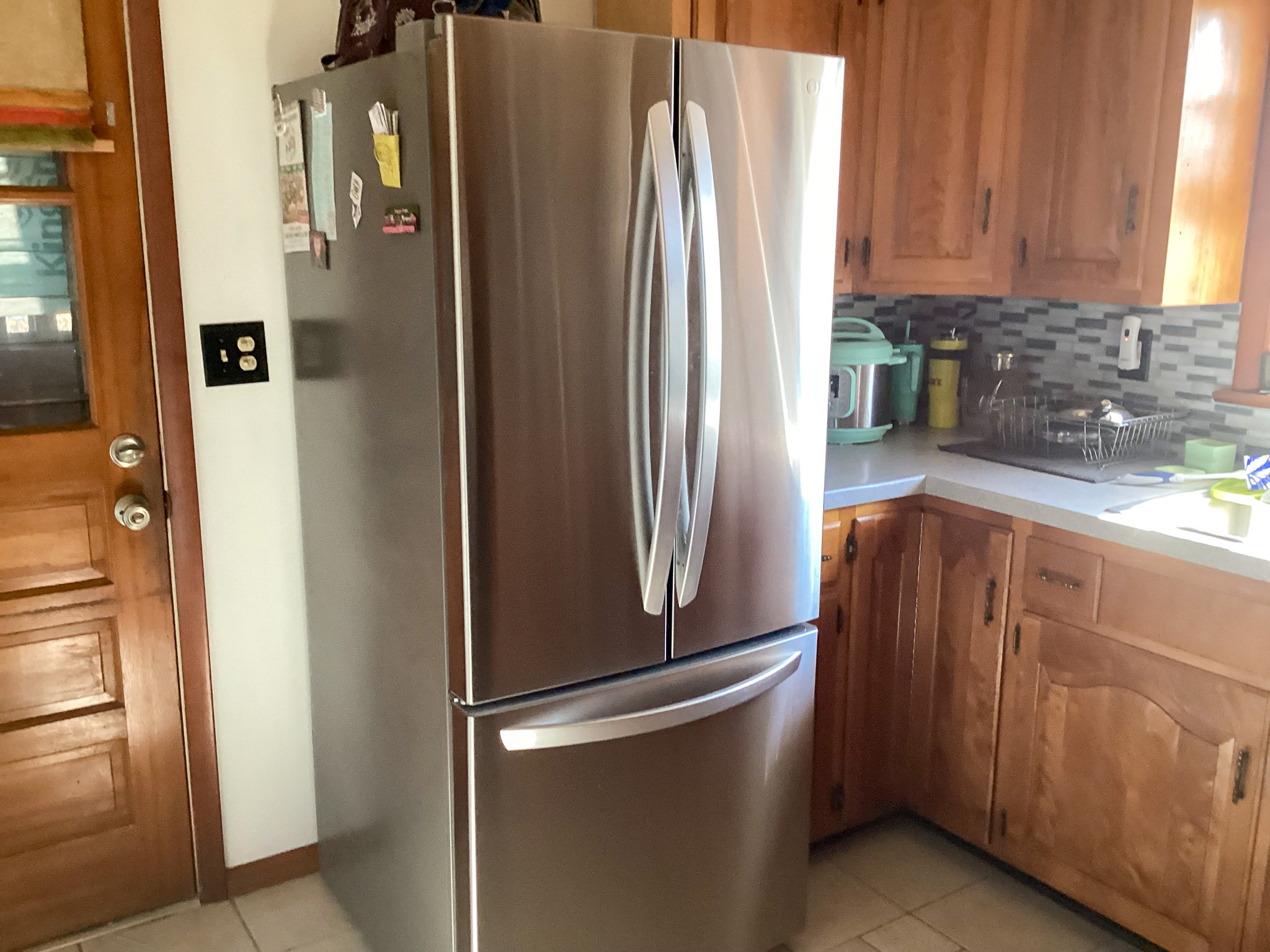 Stainless steel French‑door refrigerator beside wood cabinets and a tiled backsplash, with natural light coming in from a nearby window inside the home of Sponsored Residential Providers Bill and Heather Terry in Staunton, Virginia.