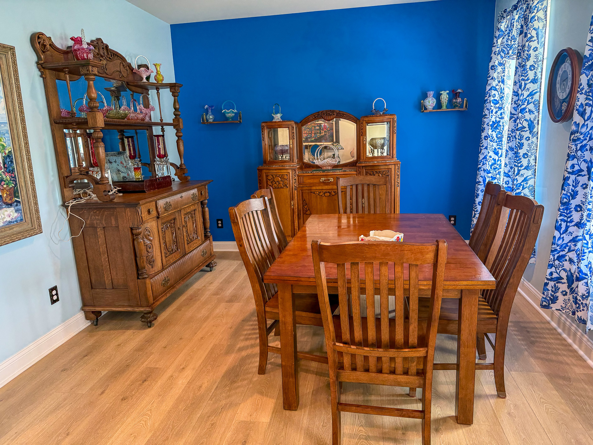 Dining room with a wooden table and chairs, blue accent wall, china cabinet, and patterned curtains inside the home of Group Home provider Traci Burch in Staurts Draft, VA.