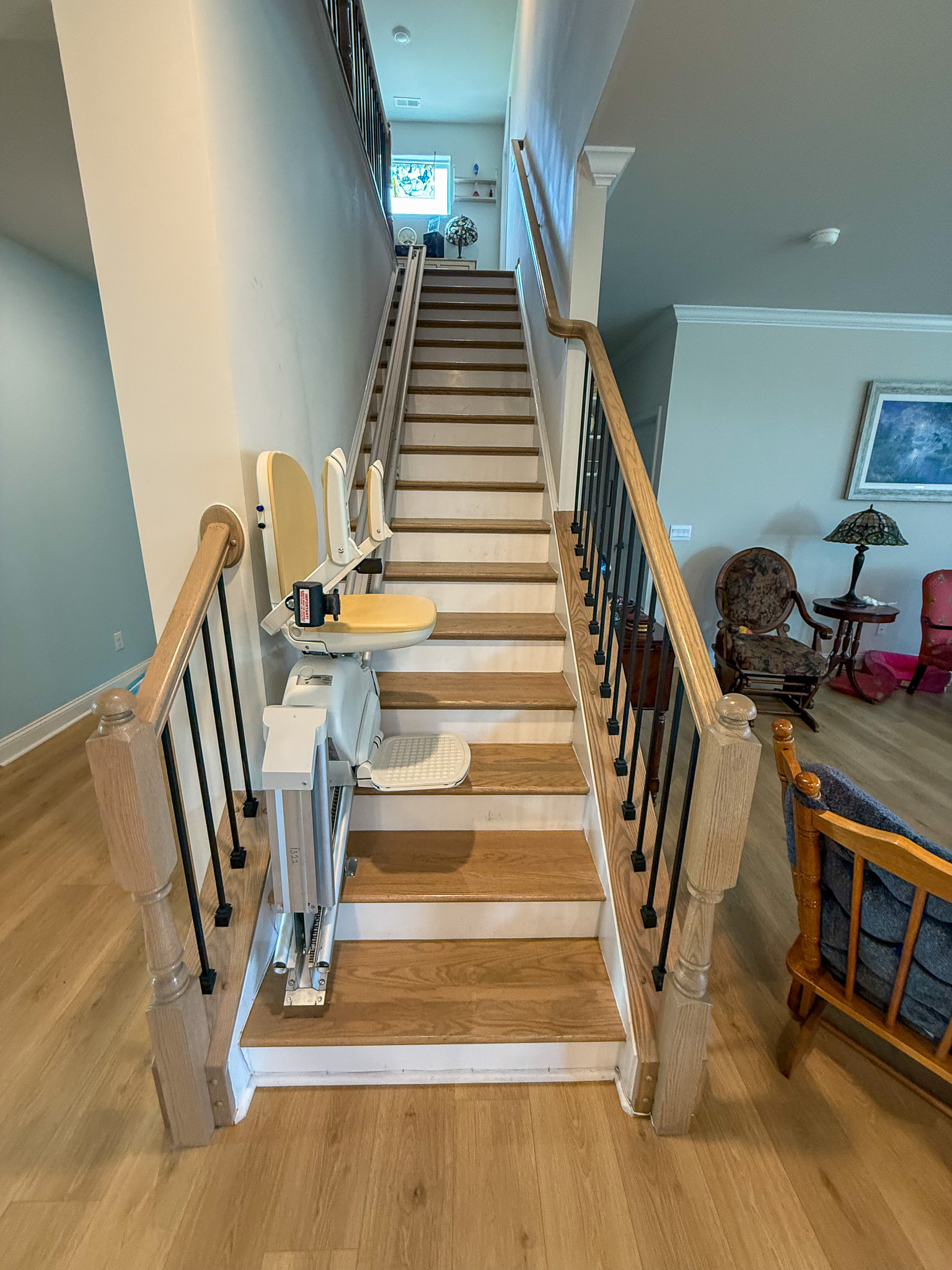 Staircase with wooden steps, railing, and a chair lift installed along the stairs inside the home of Group Home provider Traci Burch in Staurts Draft, VA.