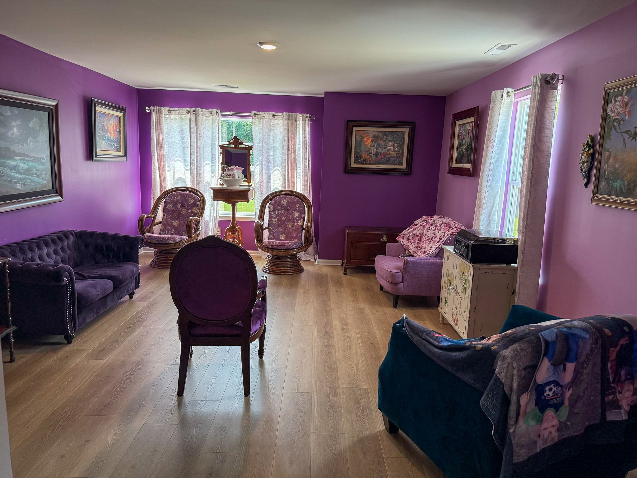 Living room with purple walls, upholstered chairs, sofa, framed artwork, and large windows inside the home of Group Home provider Traci Burch in Staurts Draft, VA.