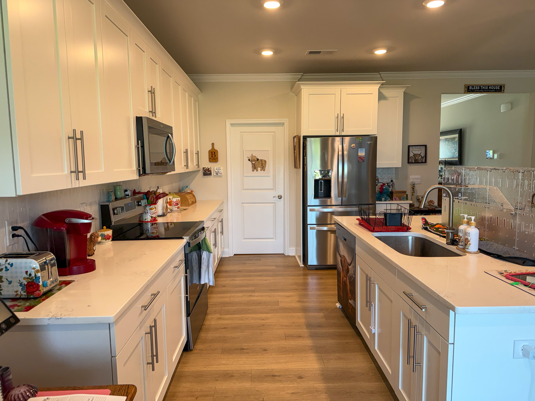 Bright kitchen with white cabinets, stainless steel appliances, center island with sink, and wood flooring inside the home of Group Home provider Traci Burch in Staurts Draft, VA.