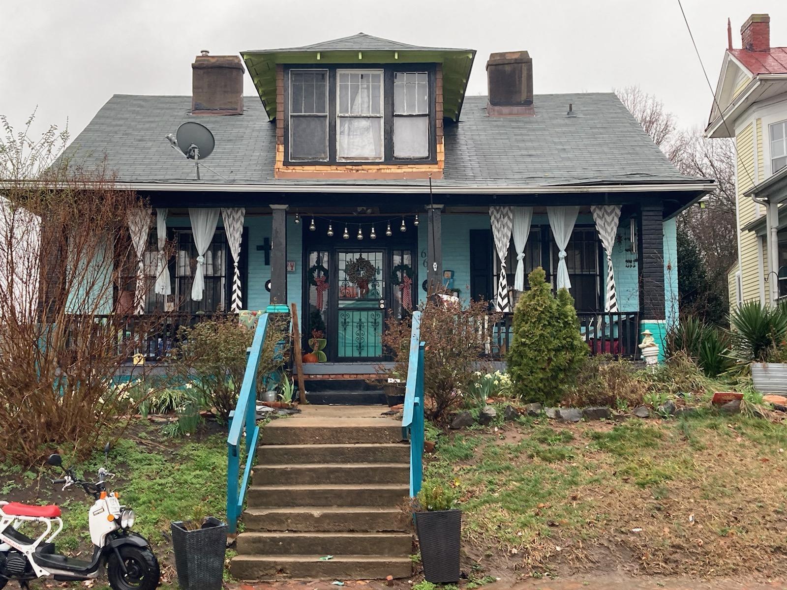 Older two‑story house with a covered front porch, teal trim, hanging decorations, and worn landscaping leading up concrete steps belonging to Sponsored Residential Provider Marcella Ajakaiye in Danville, Virginia.