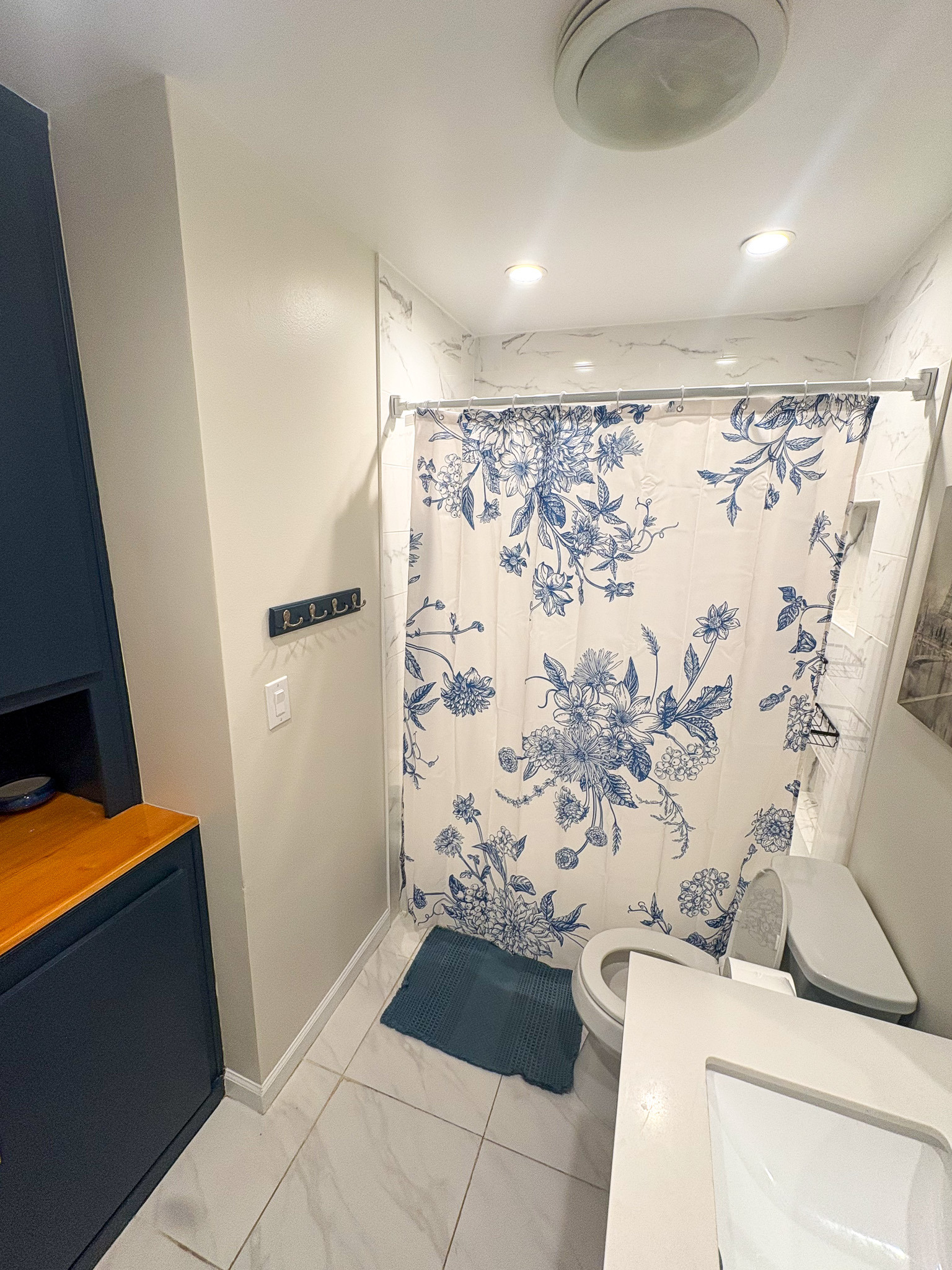 Compact bathroom with shower and blue floral curtain, white vanity and toilet, tile flooring, and recessed lighting inside the home of sponsored Residential Provider Destiny Branscome in New River Valley, VA.