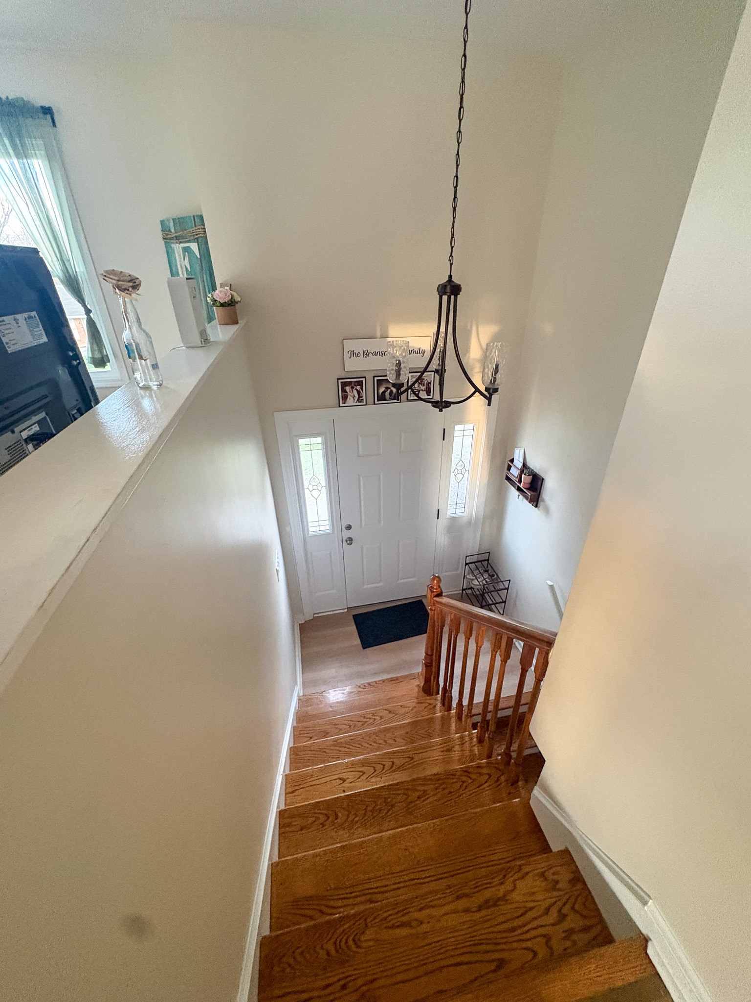 Staircase landing with wooden steps, railing, front door with sidelights, and a hanging light fixture inside the home of sponsored Residential Provider Destiny Branscome in New River Valley, VA.