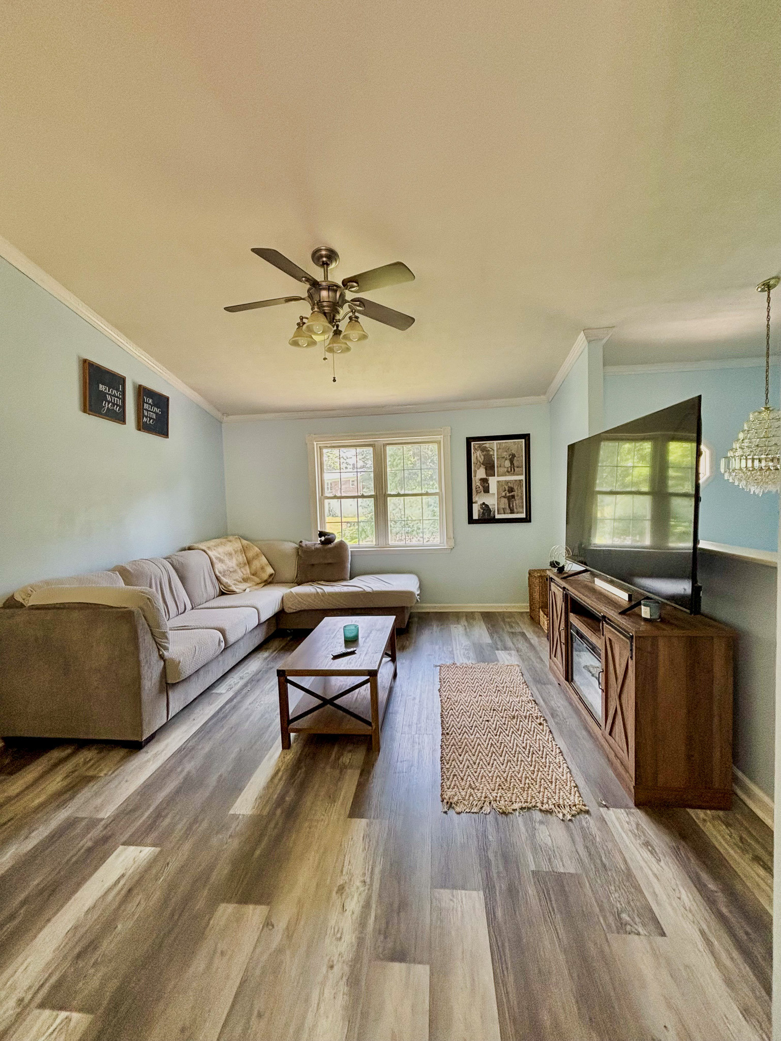 Light blue living room with sectional couch, television on stand, coffee table, ceiling fan, and large window inside the home of Sponsored Residential Provider Lana Cyzicks in Staunton, Virginia.