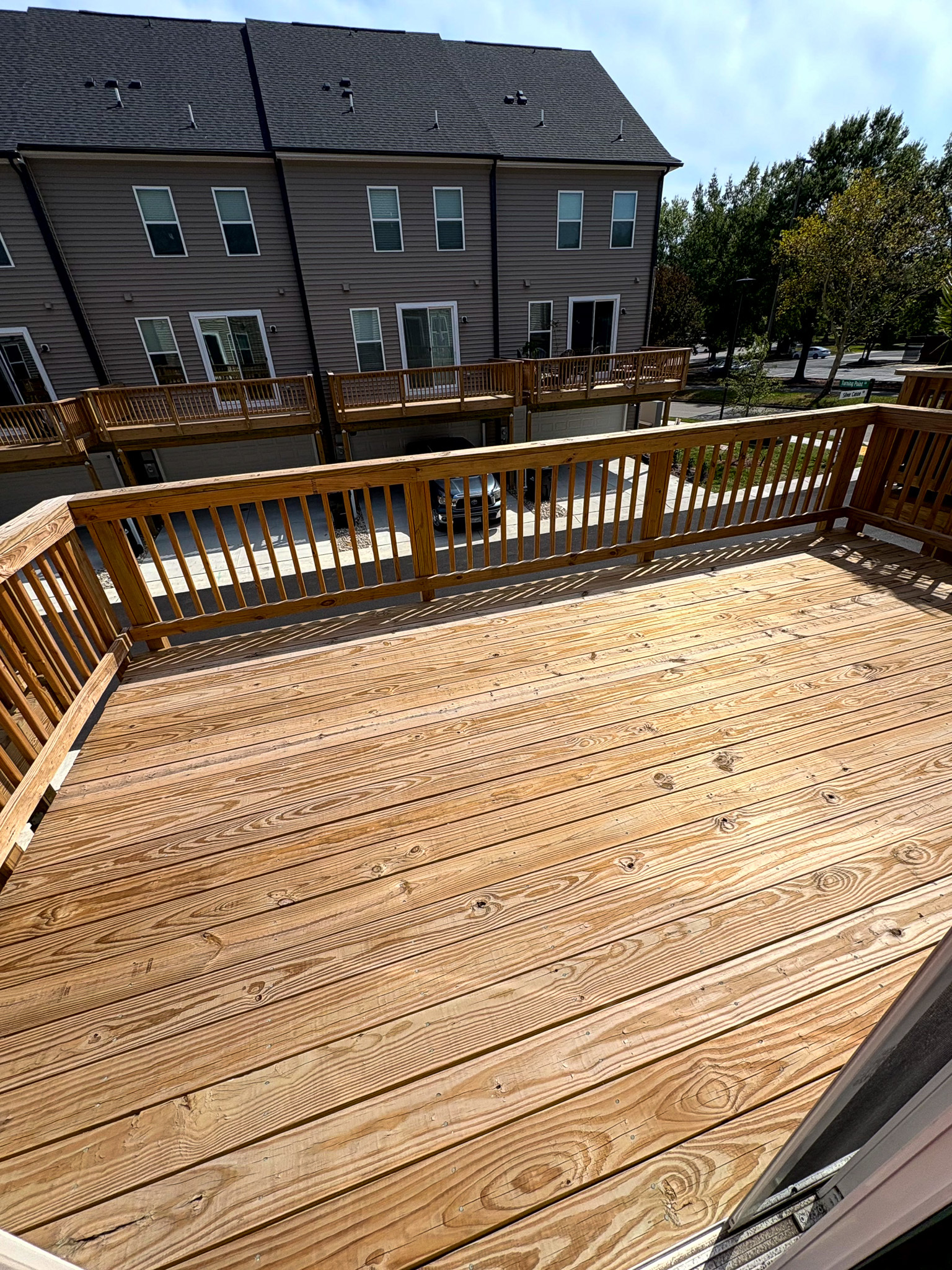 A wooden deck with railings, shown in bright sunlight, overlooking neighboring townhomes and a small parking area at the home of Sponsored Residential Providers Tania and LeSean Matthews in Glen Allen, Virginia.