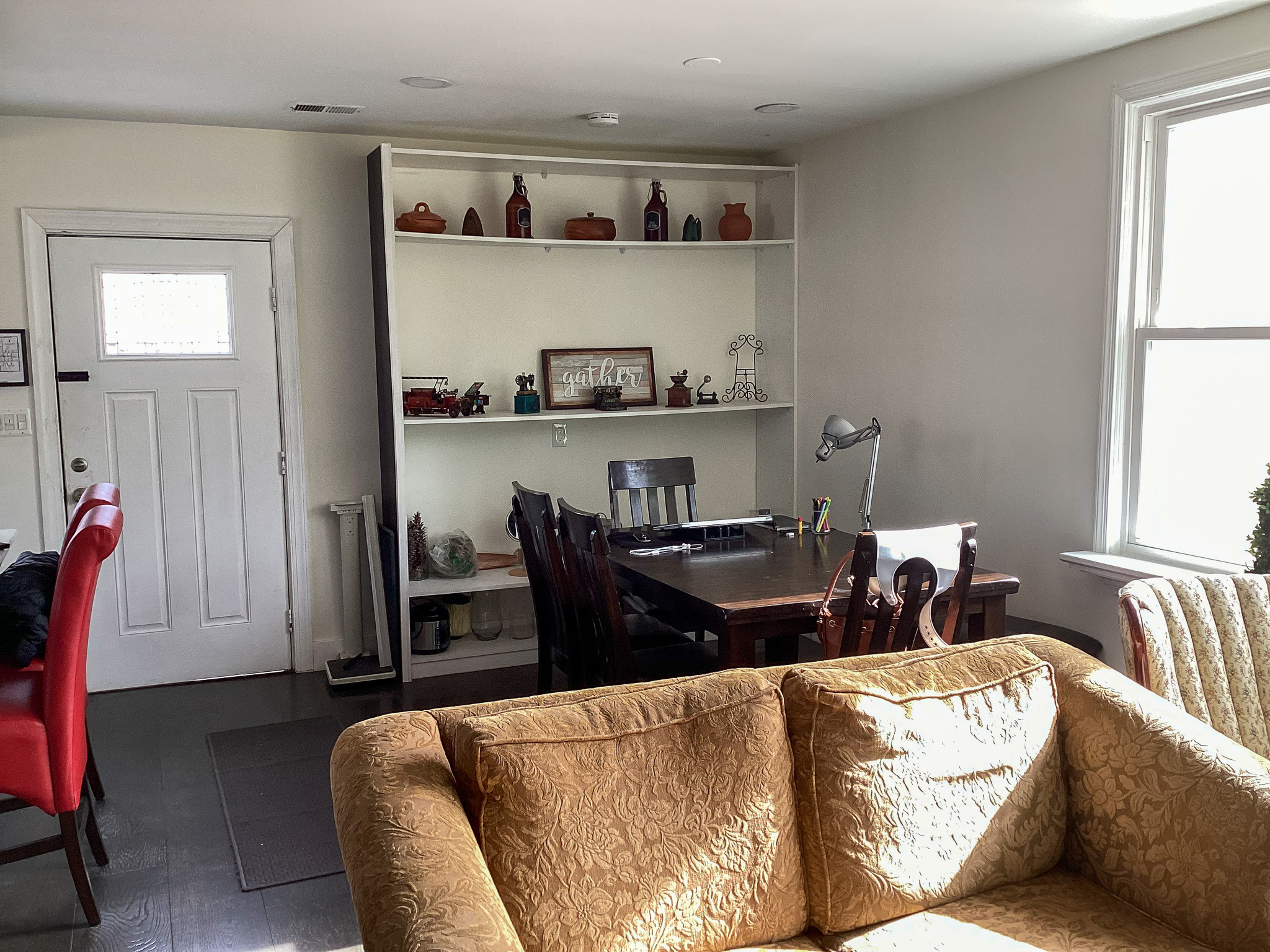 Sunlit living room with large windows, indoor plants, a red stationary bike, two red accent chairs, and a wall-mounted TV above a fireplace inside the home of Sponsored Residential Provider Eglee Escorihuela.