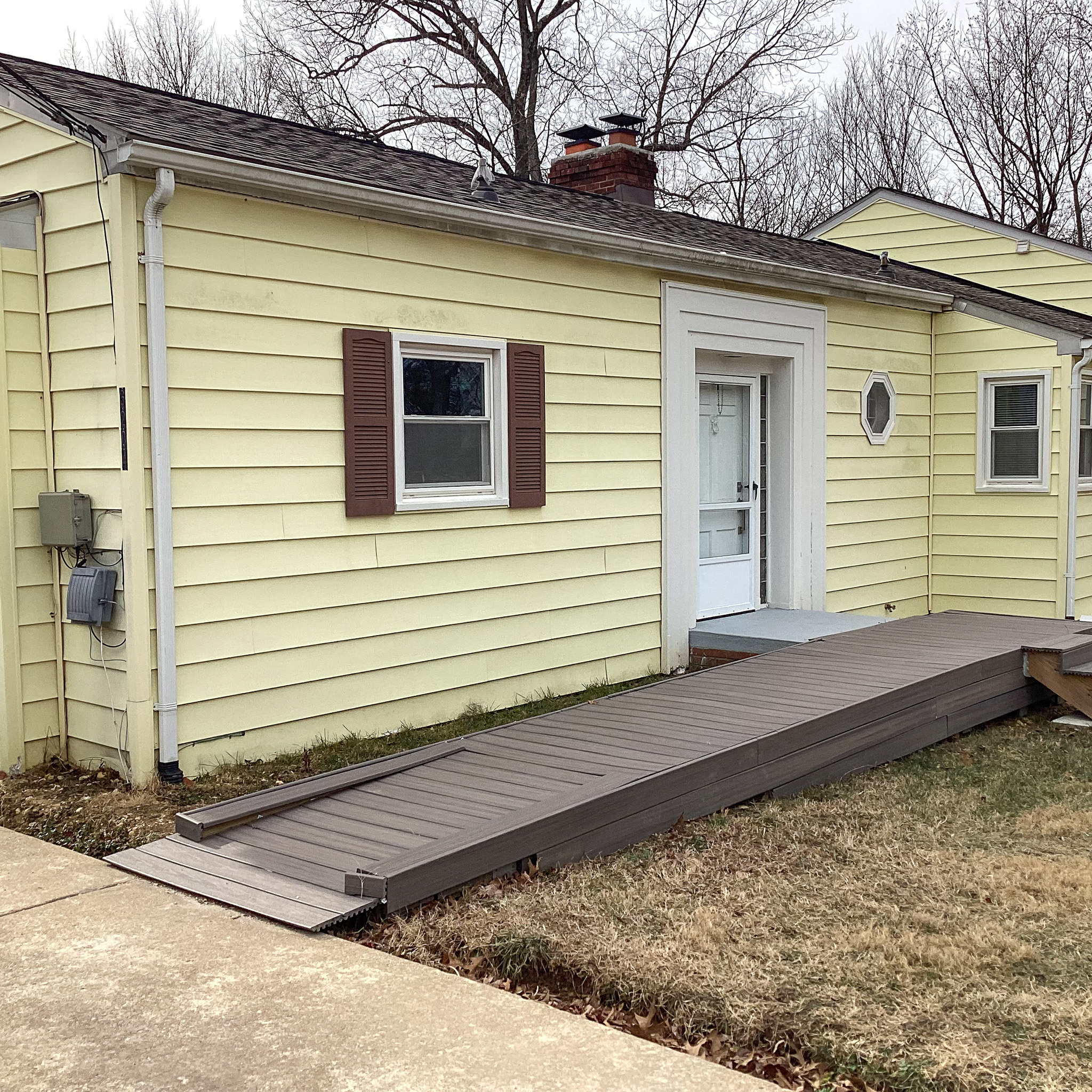 Yellow single-story house with white trim and a wooden accessibility ramp leading to the front door belonging to Sponsored Residential provider Eglee Escorihuela.