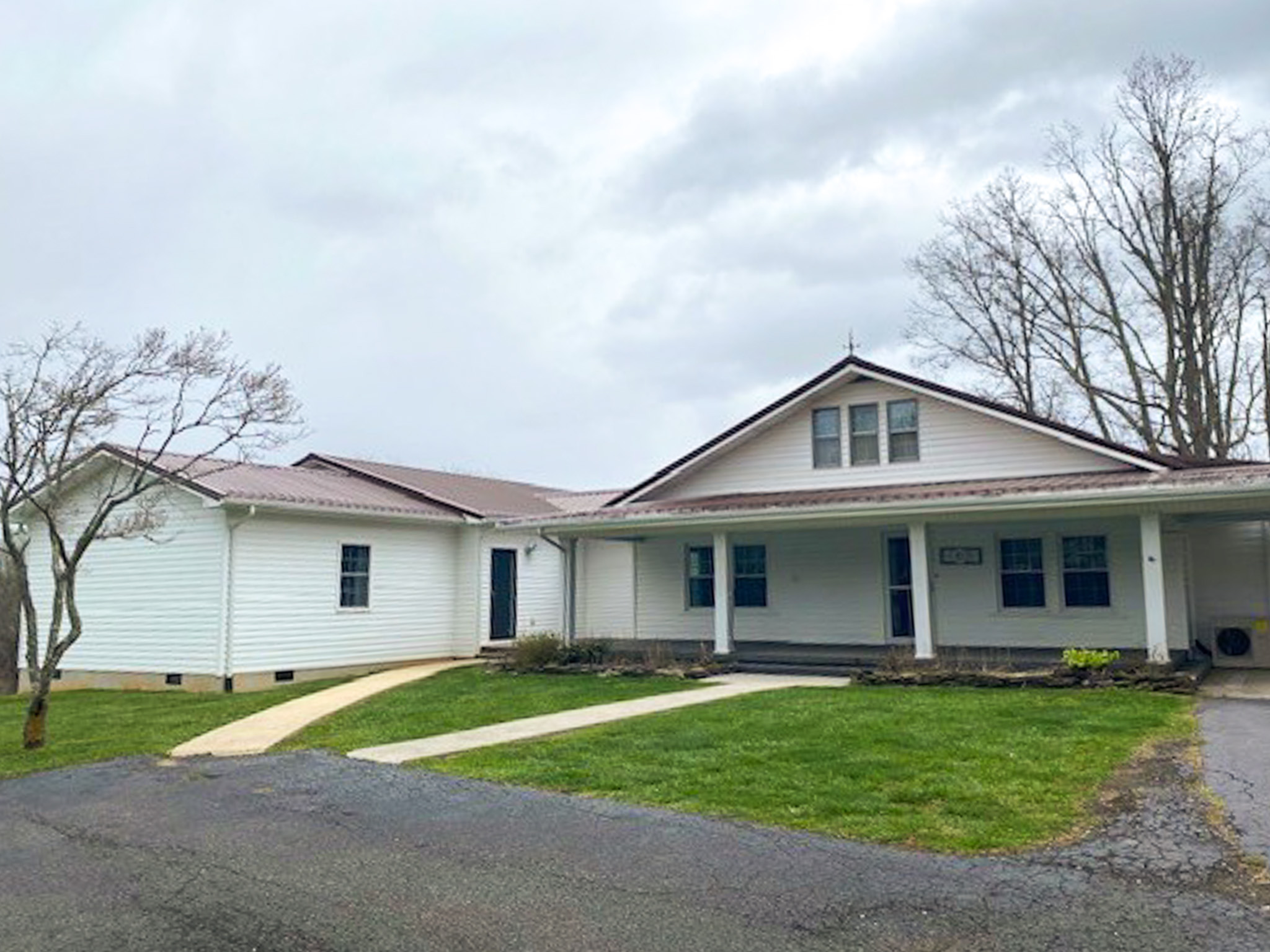 Angled view of Jake and Angie Beamer’s provider group home in Hillsville, Virginia, showing the spacious white home, covered porch, lawn, and driveway.