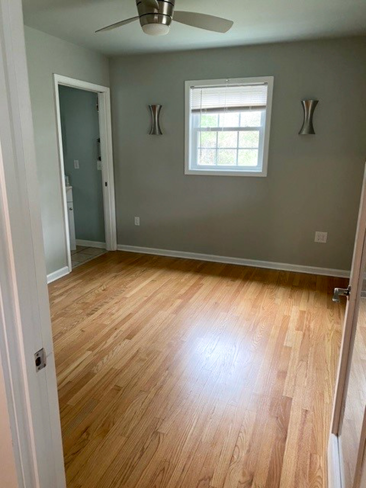 Bedroom with hardwood floors, neutral gray walls, a ceiling fan, and an attached bathroom inside Jake and Angie Beamer’s provider group home in Hillsville, Virginia.