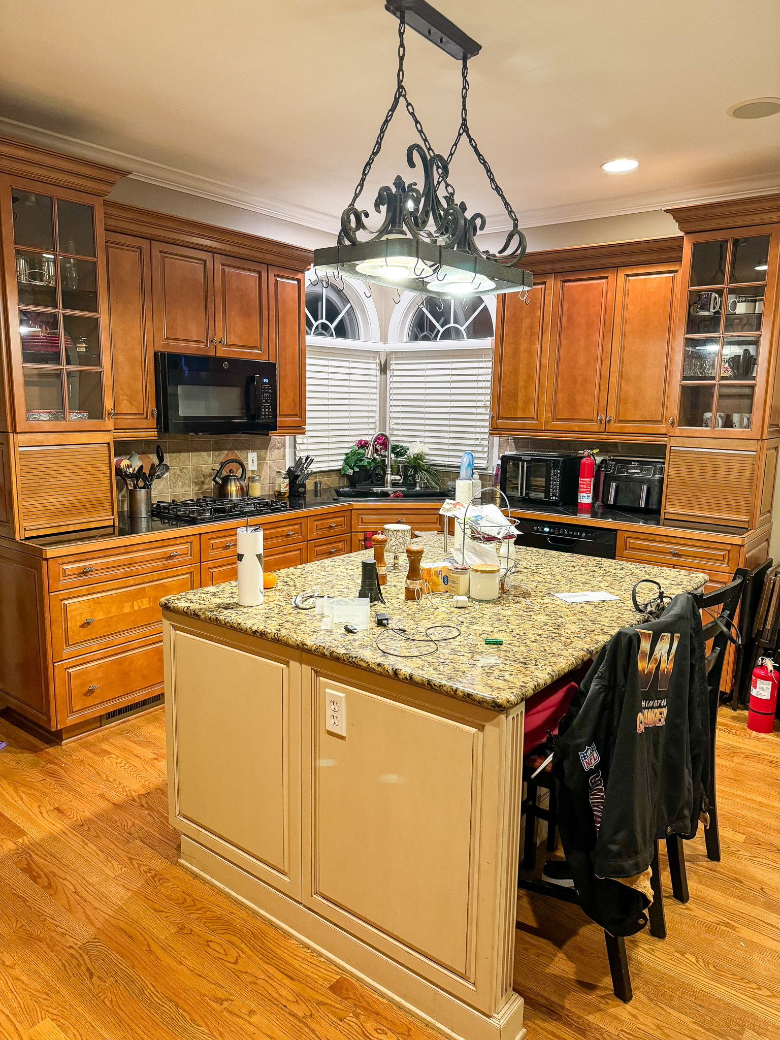 A kitchen with wooden cabinets, a granite‑top island, black chairs, and a decorative wrought‑iron light fixture overhead inside the home of Sponsored Residential Provider Sharon Jennings in Salem, Virginia.