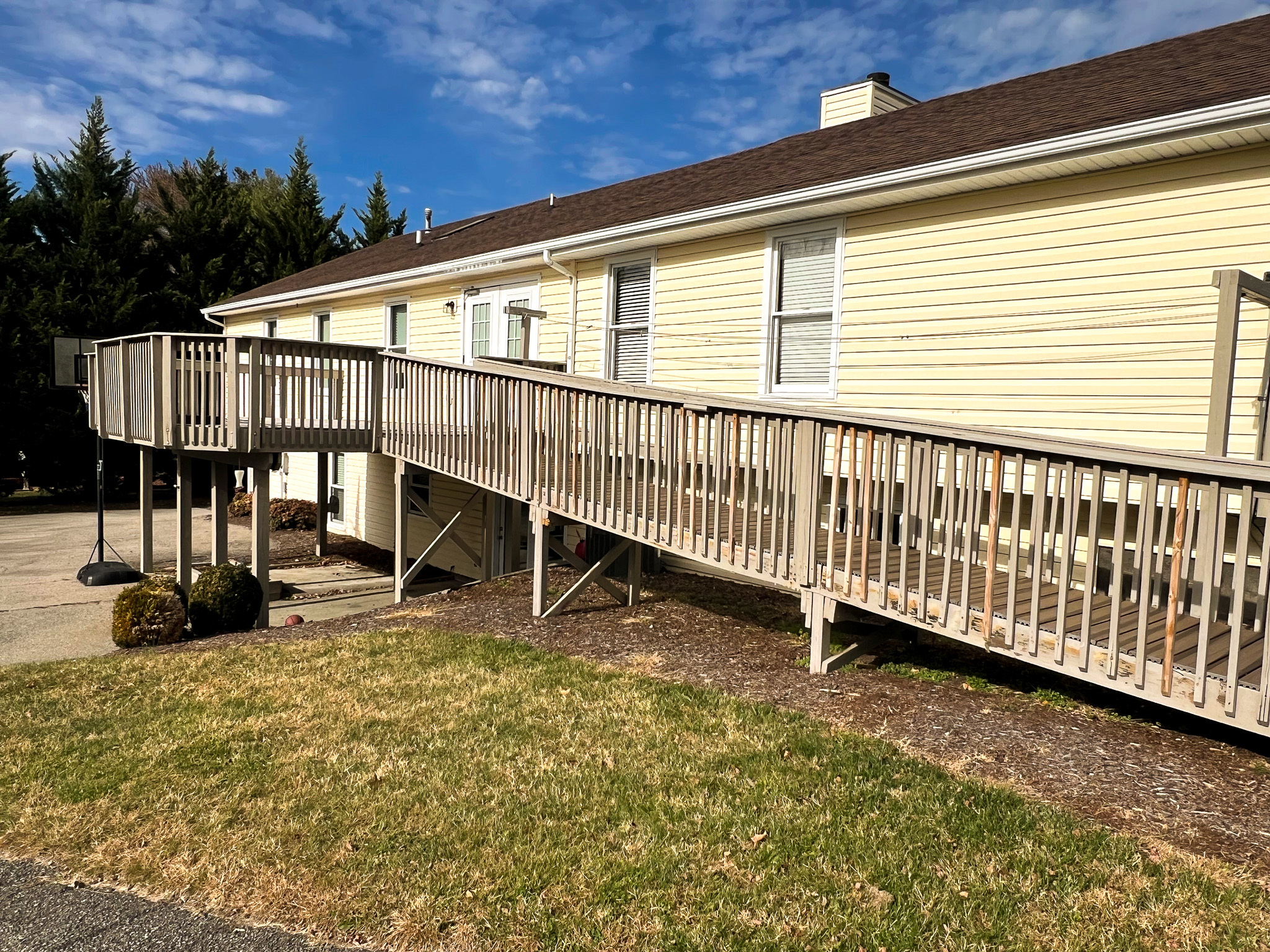 A yellow house with a long wooden accessibility ramp extending from the side deck to the driveway belonging to Group Home Providers Anthony and Melissa Johnson in Daleville, Virginia.