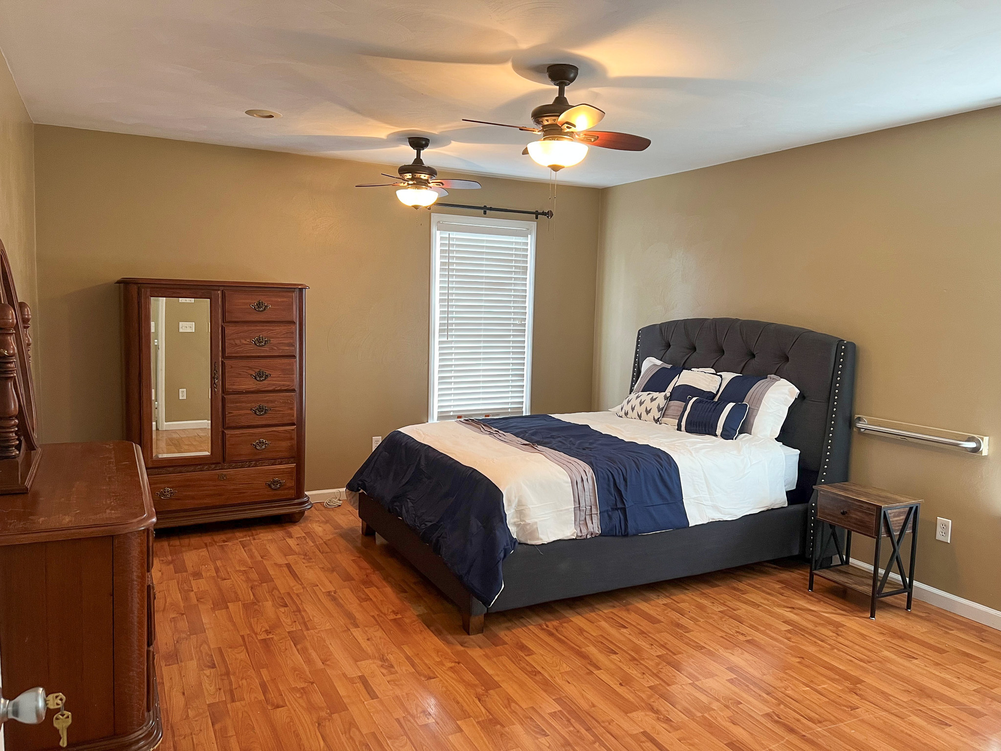 A bedroom with beige walls, a metal bed frame with yellow-accented bedding, built‑in shelves, and a ceiling fan with a light  inside the home of Group Home Providers Anthony and Melissa Johnson in Daleville, Virginia.