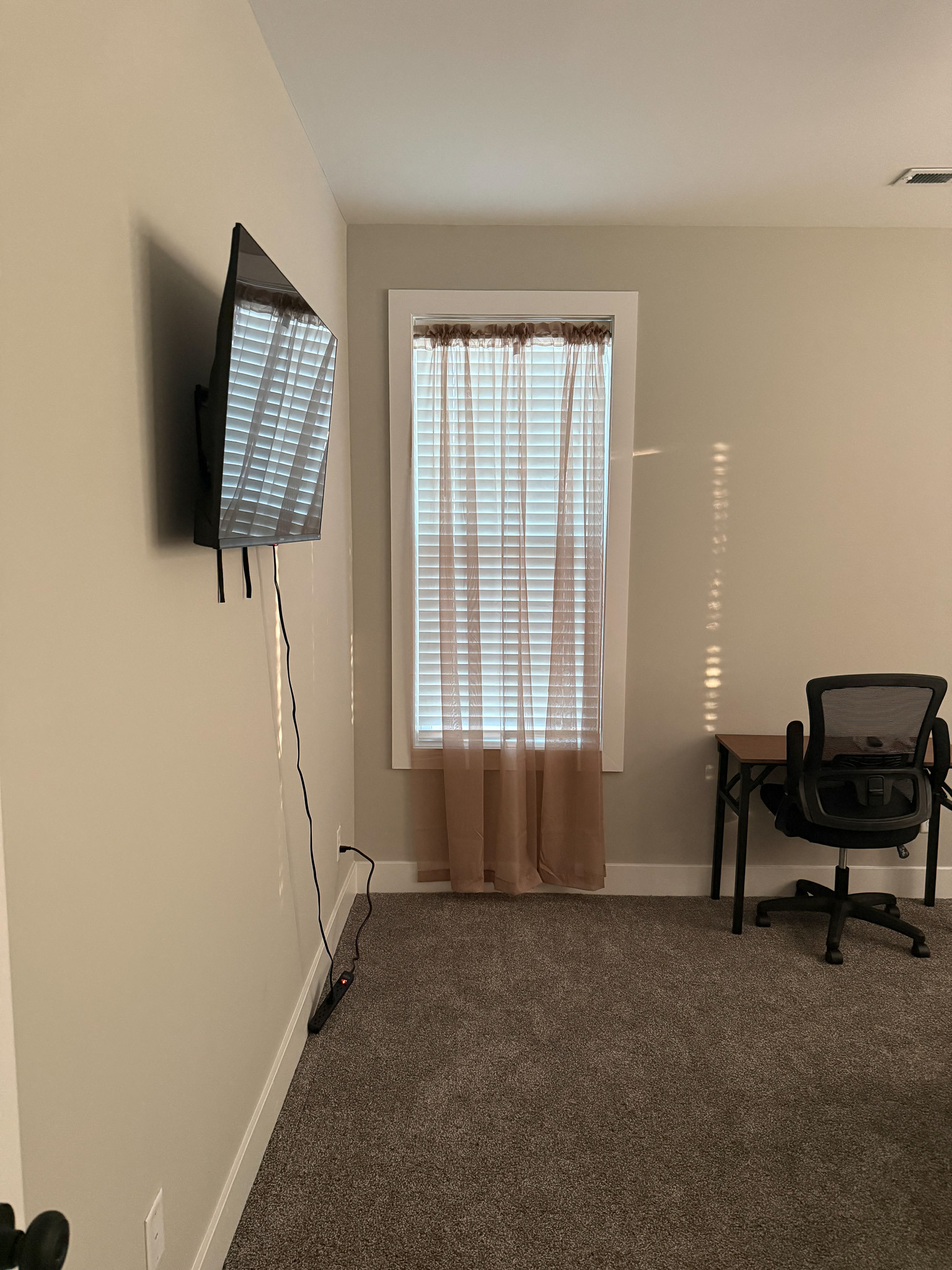 Modern bedroom with a wall-mounted TV, desk, and large window in the home of Sponsored Residential Provider Justina Megginson in Roanoke, Virginia.