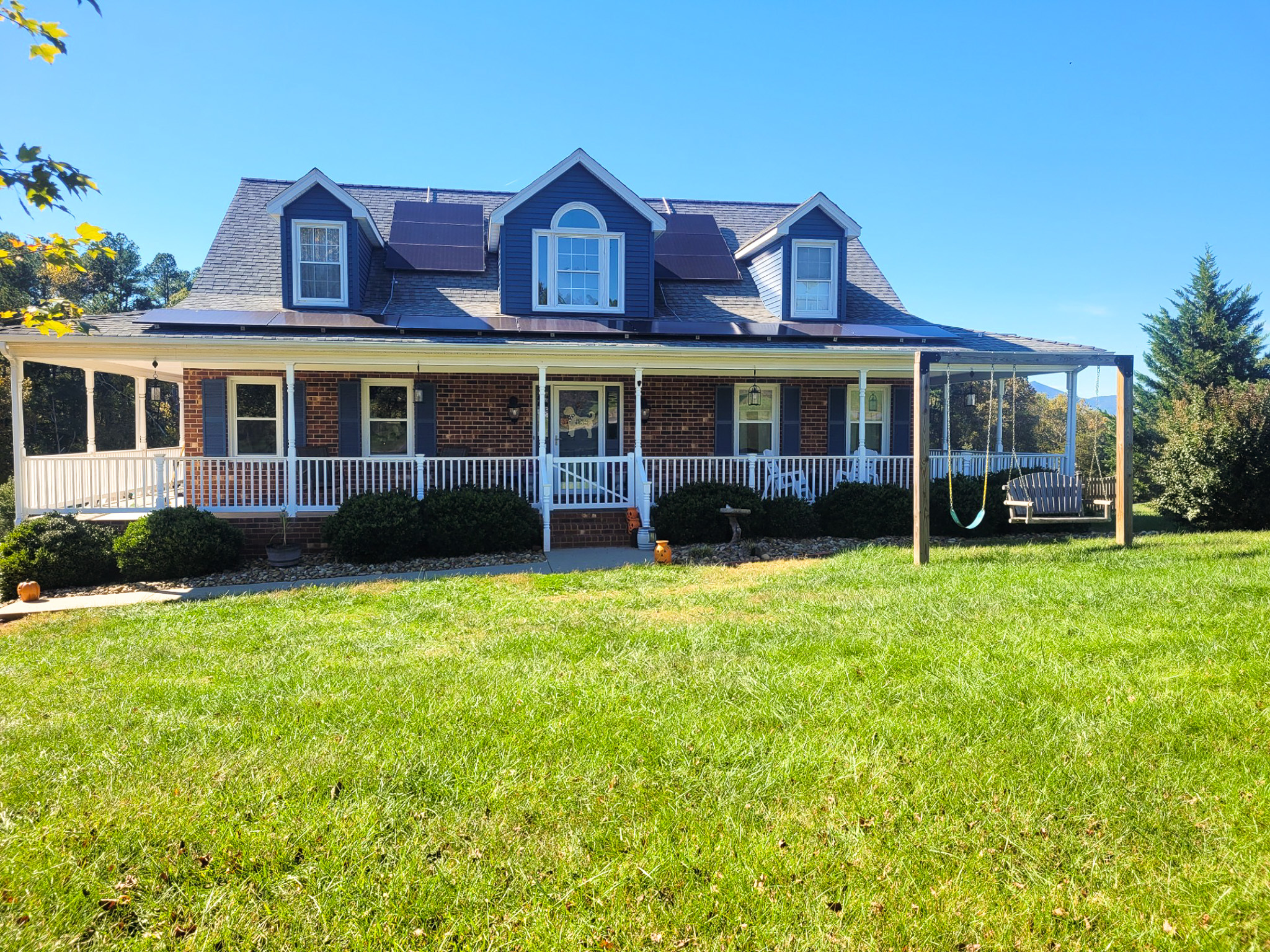 Brick house with a large wraparound porch, dormer windows, and a wide grassy lawn belonging to Sponsored Residential Provider Karen Betham in Goode, Virginia.