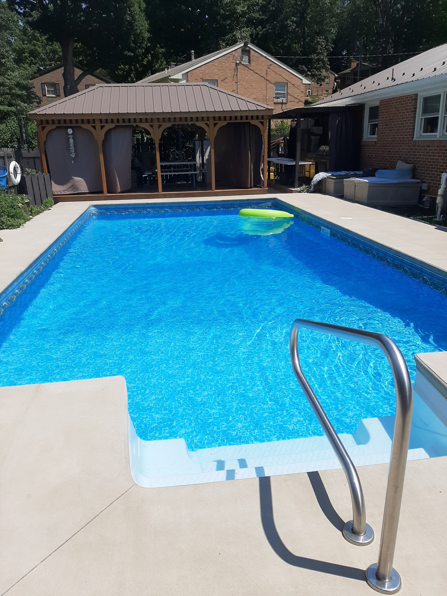 Backyard swimming pool with steps, metal handrail, floating pool toy, and covered pavilion nearby belonging to Sponsored Residential Provider Rhonda Kestner in Staunton, VA.