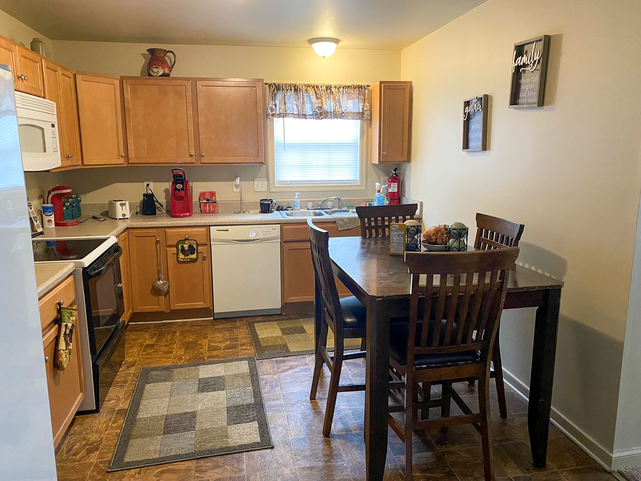 A kitchen with wooden cabinets, standard appliances, and a dining table with four chairs in the center of the room inside the home of Sponsored Residential Providers Xaiver Heath and David Williams in Richmond, Virginia.