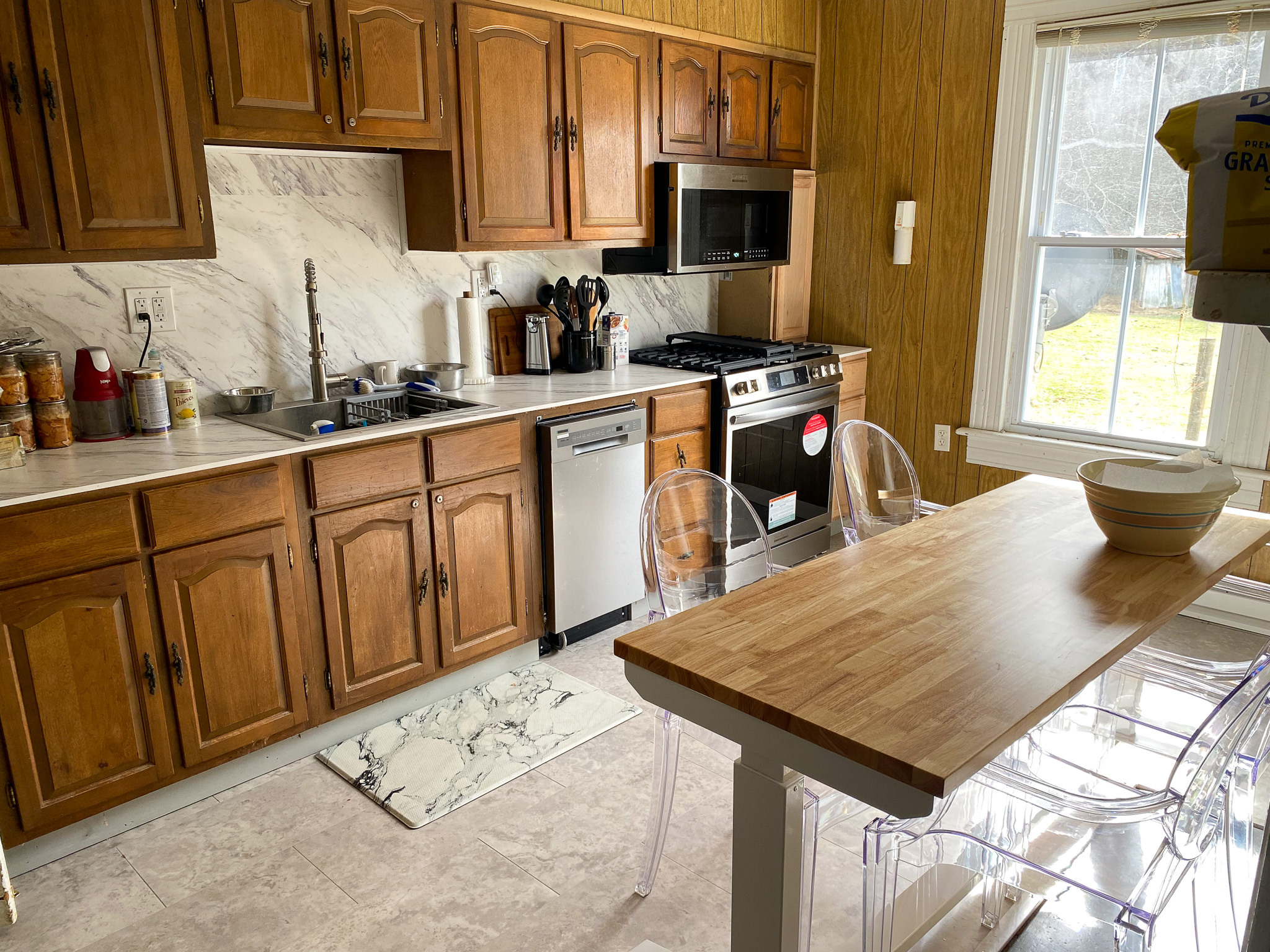 Kitchen with wood cabinets, gas stove, dishwasher, marble-look backsplash, and small island table inside the home of Sponsored Residential Providers Barbara and Larry Hatcher in Floyd, Virginia.