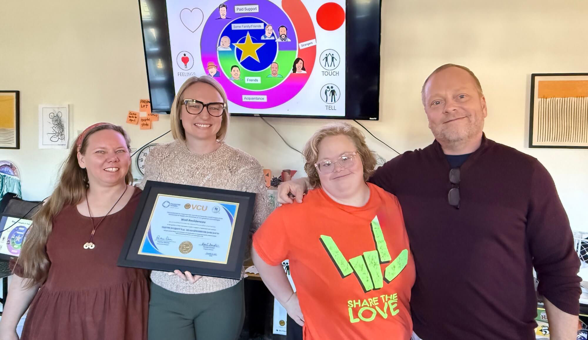 Four people celebrate Wall’s LEAP certification holding a recognition certificate at an event