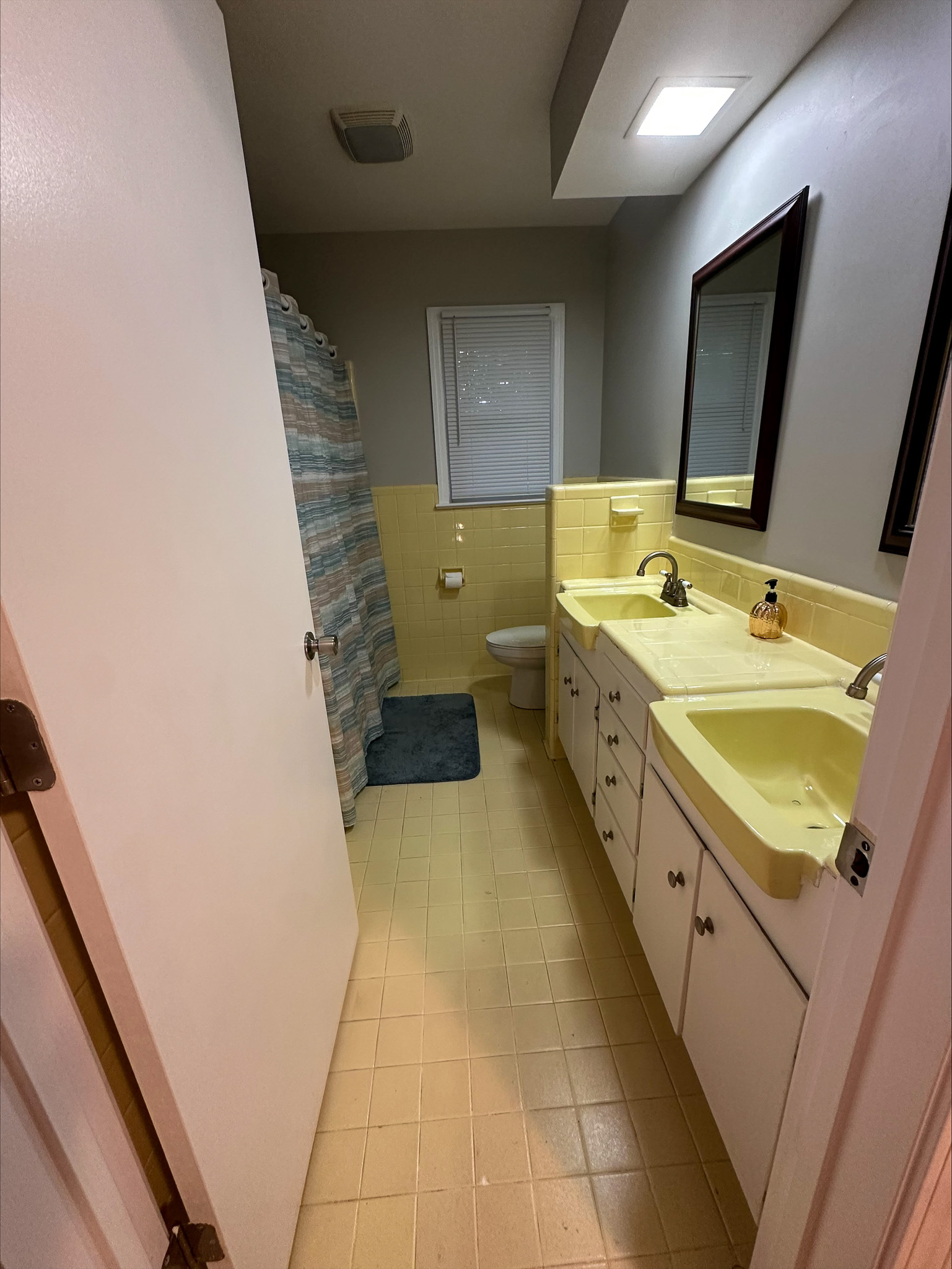 A narrow bathroom with yellow countertops, dual sinks, white cabinets, and a shower at the far end inside the home of Group Home Provider Tina Langhorn in Roanoke, Virginia.