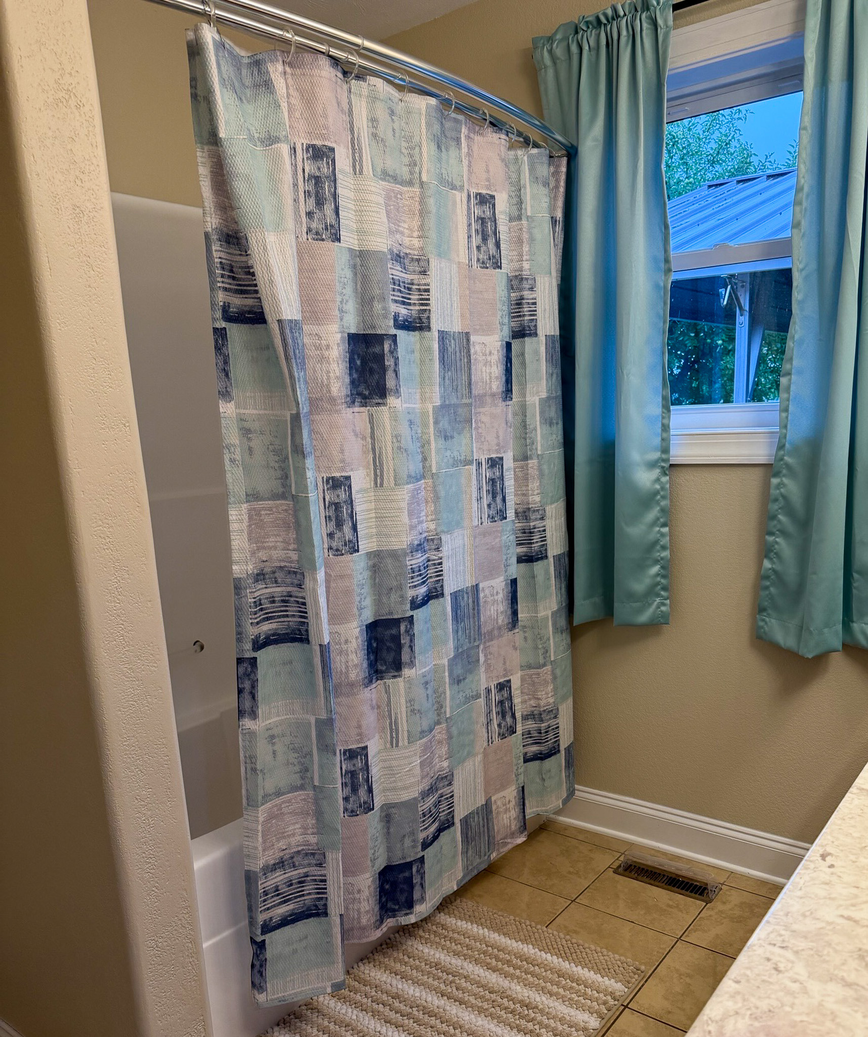 Bathroom with a tub-shower combination, patterned shower curtain, and window with blue curtains in the home of Wall Group Home provider Lisa Lohr in Harrisonburg, VA
