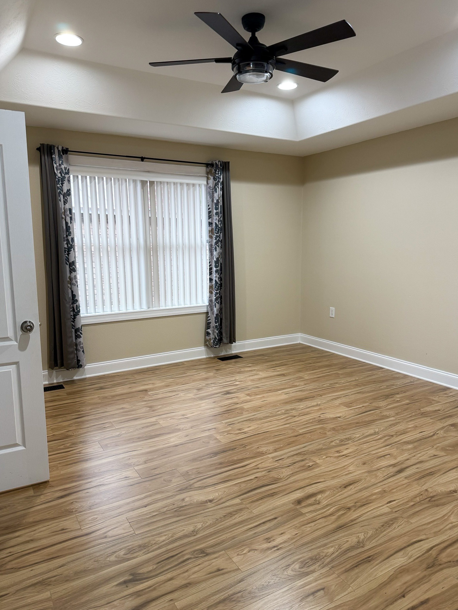 Bright bedroom with wood flooring, a tray ceiling, ceiling fan, and large window in the home of Wall Group Home provider Lisa Lohr in Harrisonburg, VA.