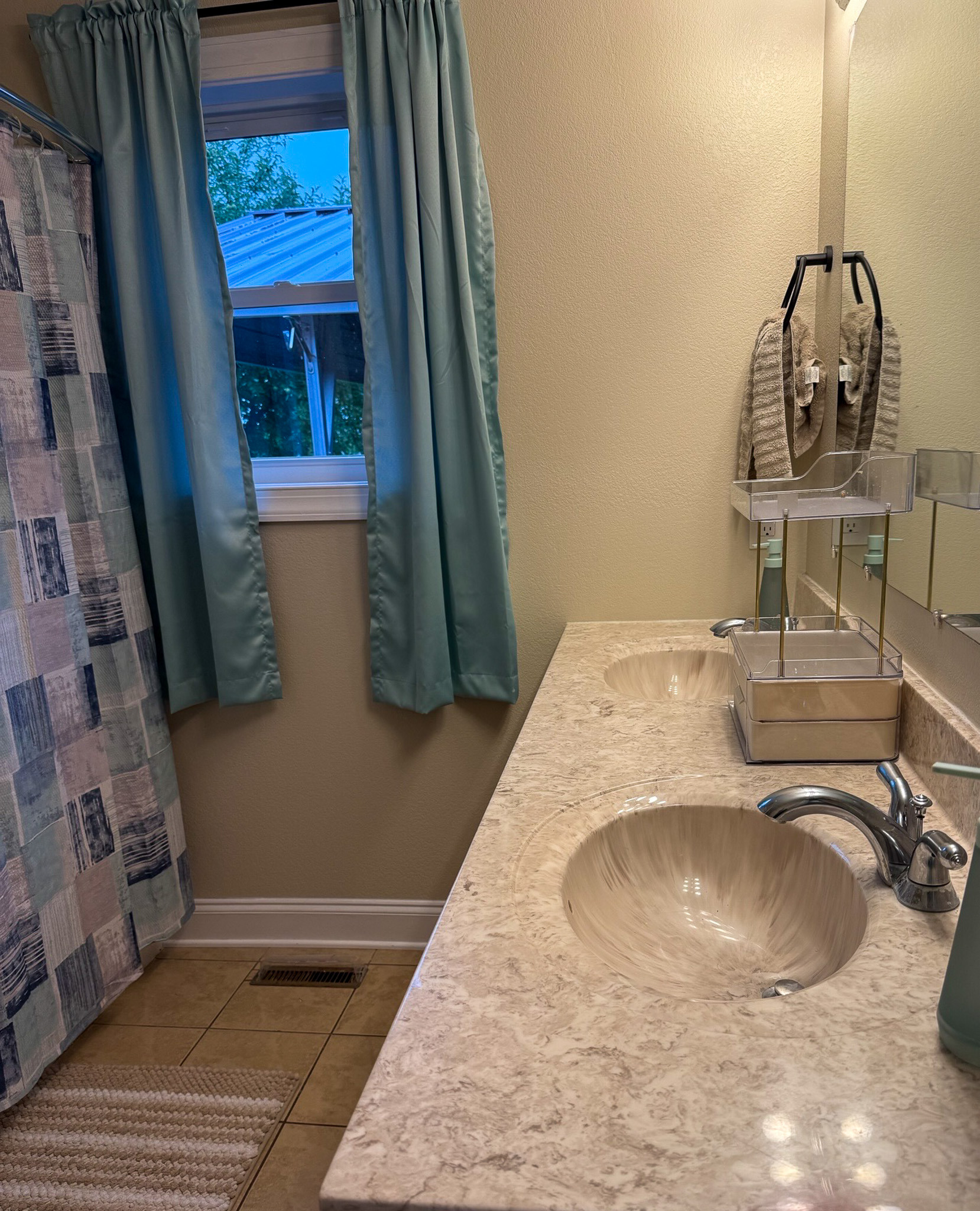 Bathroom with a double-sink vanity, shower, and window with blue curtains in the home of Wall Group Home provider Lisa Lohr in Harrisonburg, VA.