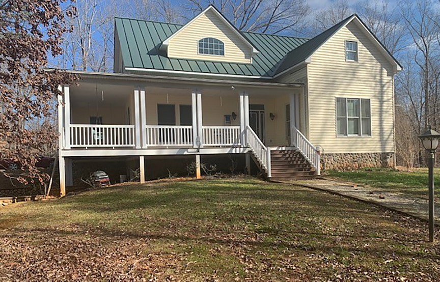Two‑story light‑yellow house with a green metal roof and a wide front porch facing a grassy yard belonging to Group Home Providers Felicia and Jason Martin in Amherst, Virginia.