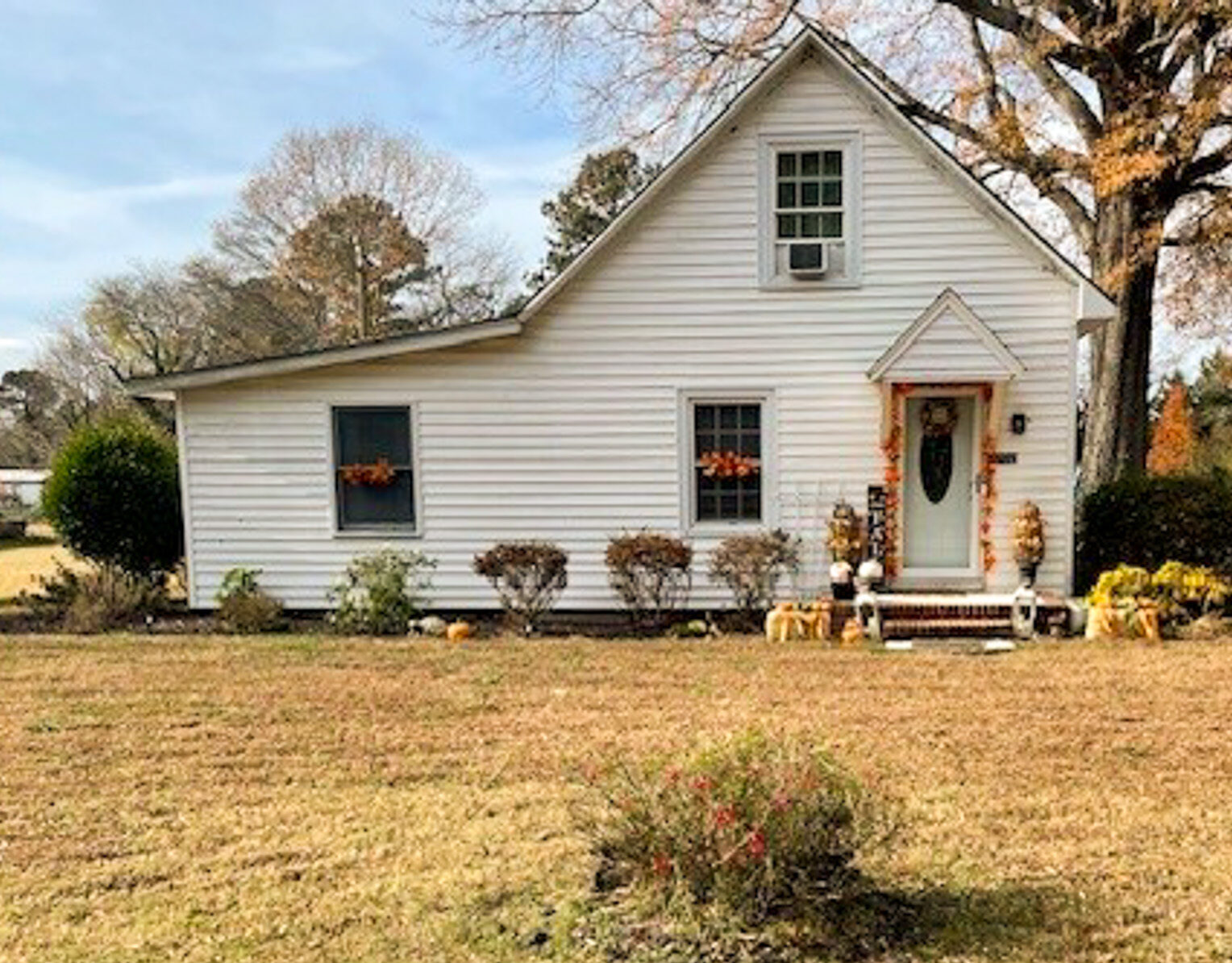 A small white two‑story house with a steep roof, front porch, and autumn decorations, set on a large grassy yard with shrubs and trees belonging to Sponsored Residential provider Michelle Willis in Hayes, Virginia.