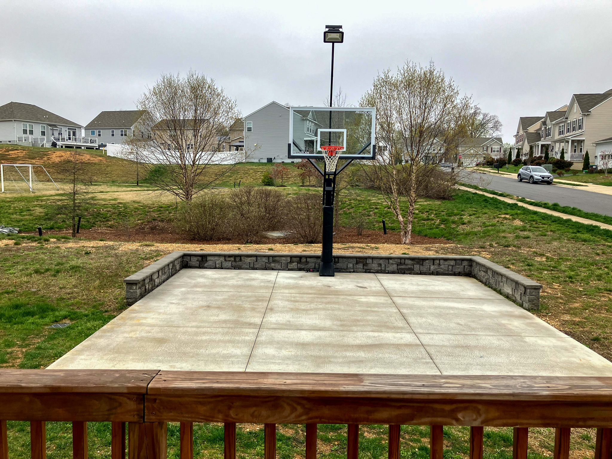 A backyard concrete basketball court with a hoop, viewed from a wooden deck, with neighboring houses in the background outside the home of Sponsored Residential Providers Torwon and Deljuan Mitchell in Fredericksburg, Virginia.