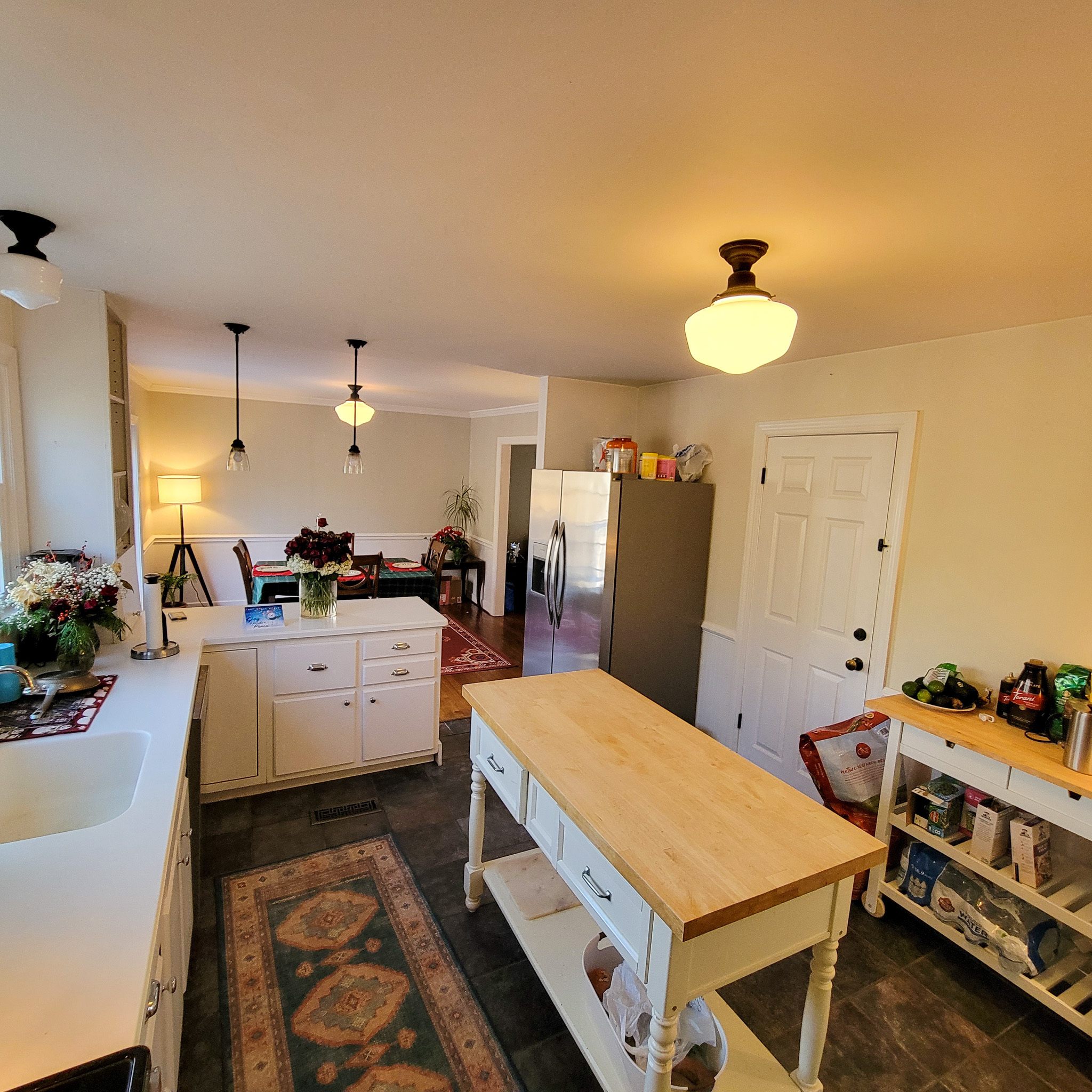 Kitchen with white cabinets, a center island with a wood countertop, and a view into a living area with lamps and seating inside the home of Group Home Provider Jared Nepal in Fredericksburg, Virginia.