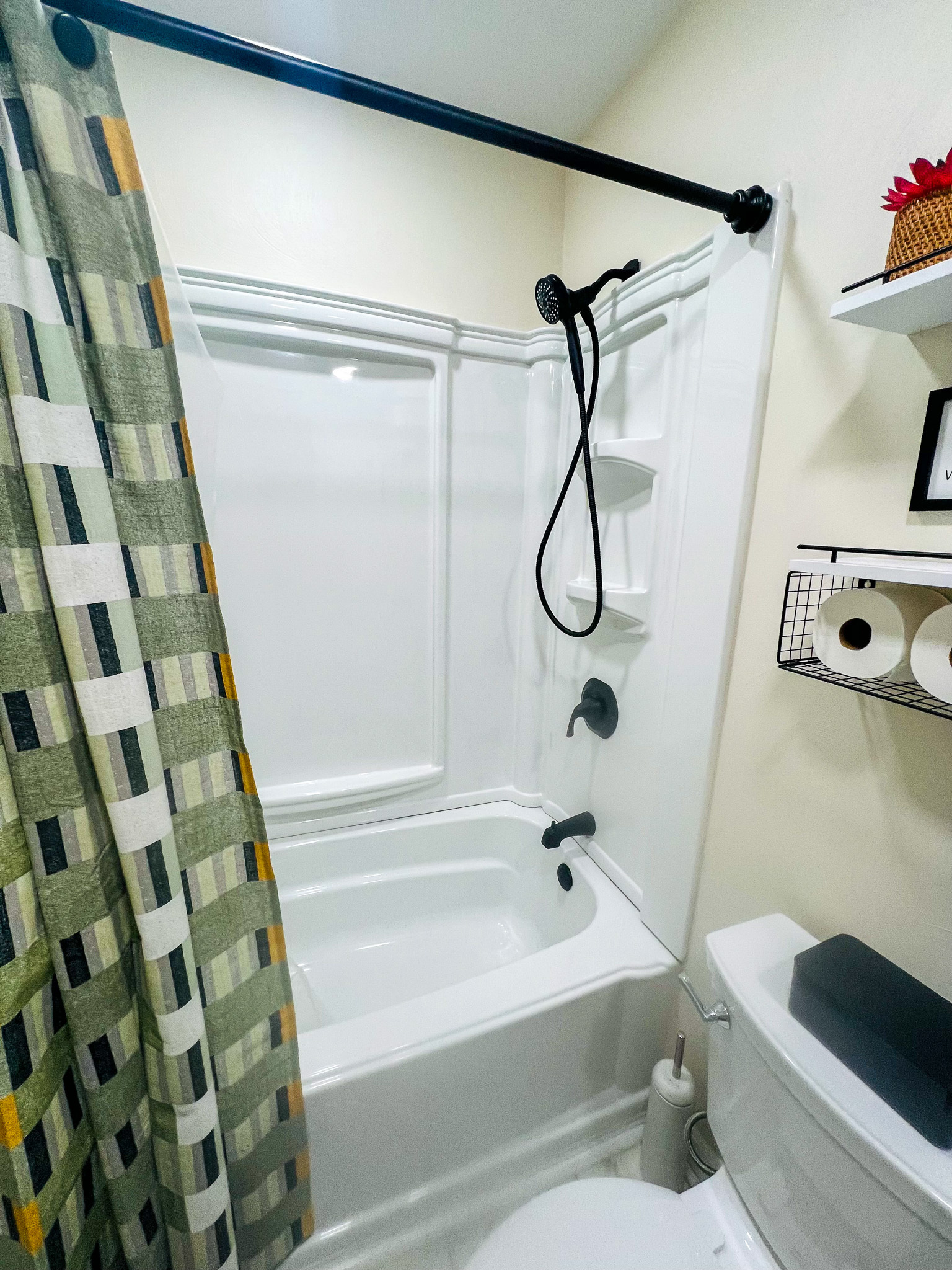 A shower‑tub combo with a patterned curtain, white walls, and black fixtures inside the home of sponsored residential provider Regina Hill in Roanoke, Virginia.