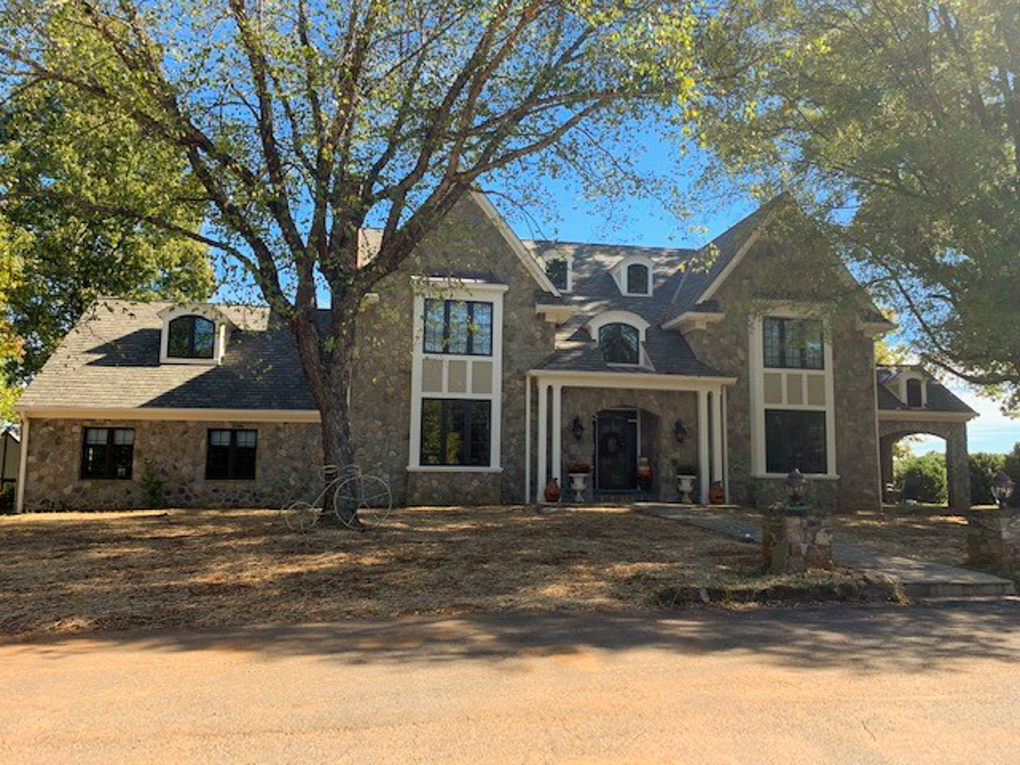 Large stone house with multiple gables, dormer windows, and a covered front entrance shaded by tall trees belonging to Group Home Providers Rhonda and Bruce Norconk in Amherst, Virginia.