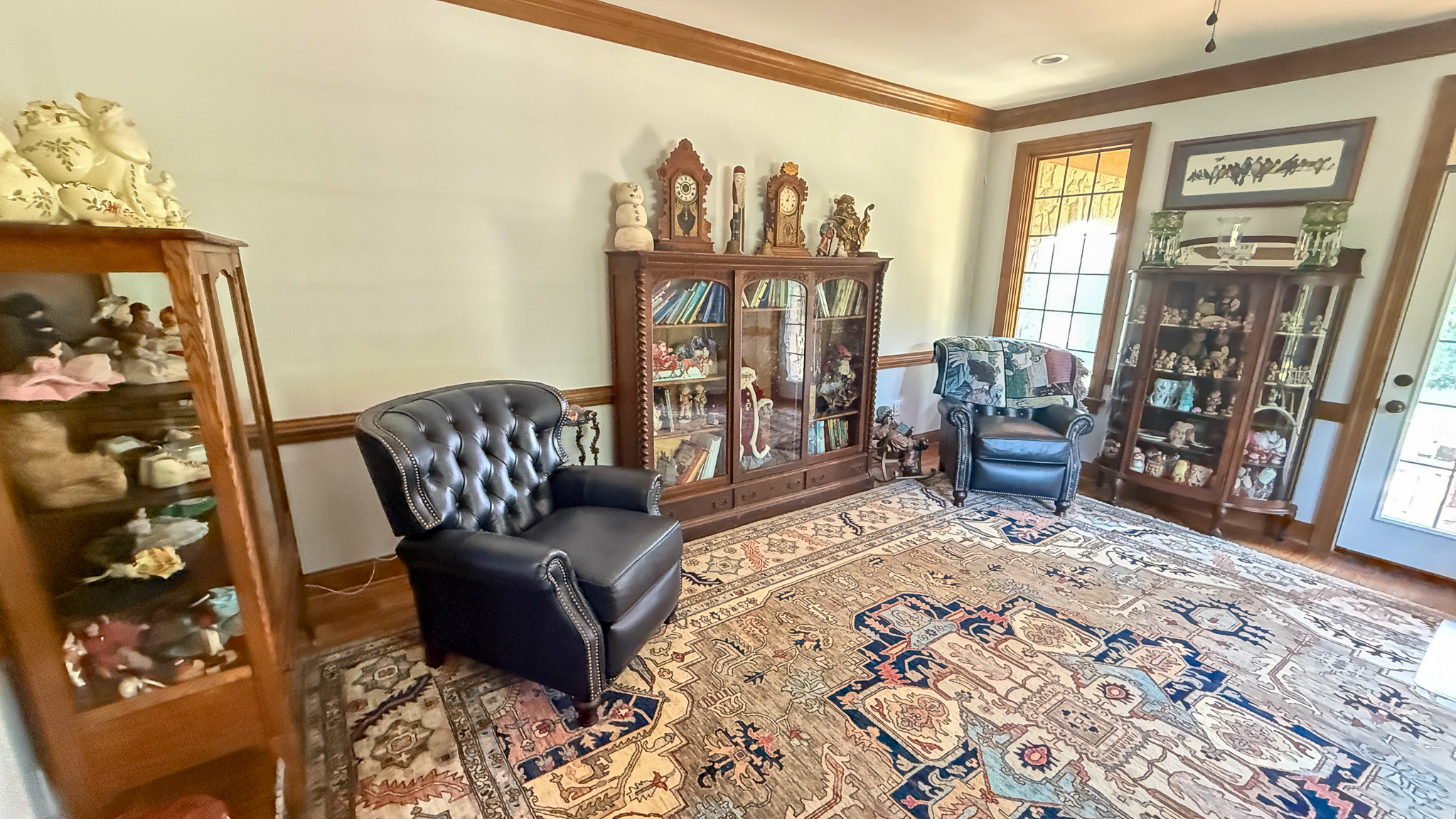 Sitting room with display cabinets of collectibles, leather chairs, and a patterned area rug  inside the home of Group home providers Rhonda and Bruce Norconk in Lynchburg, VA.