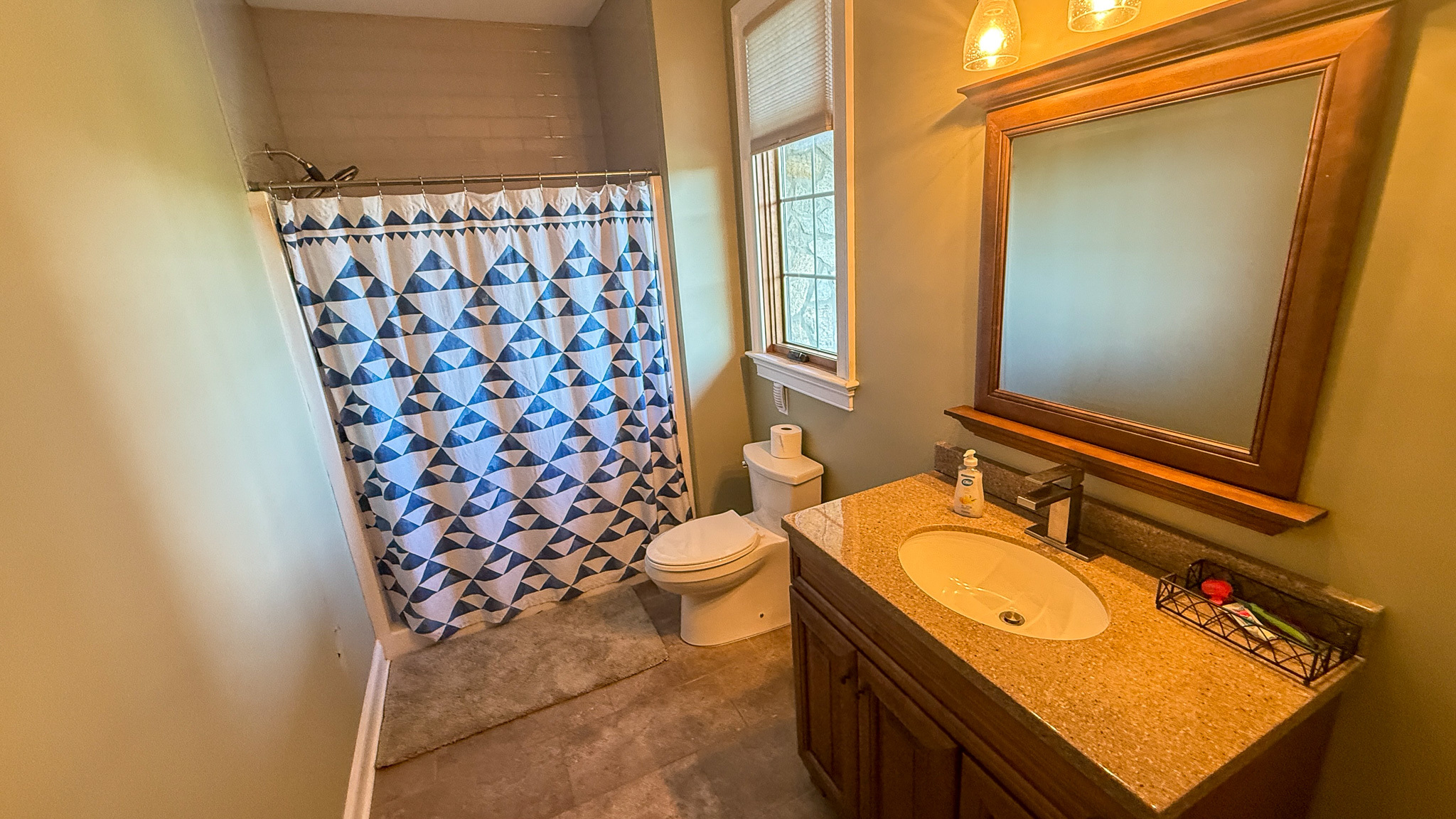 Bathroom with shower, toilet, and vanity with a large framed mirror inside the home of Group home providers Rhonda and Bruce Norconk in Lynchburg, VA.