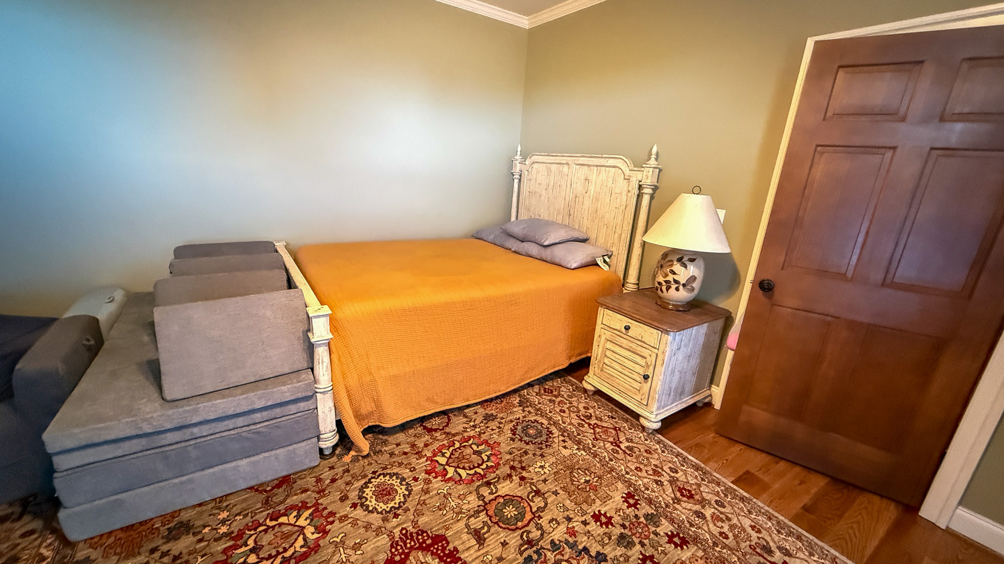 Bedroom with a bed, patterned rug, and dresser with a TV inside the home of Group home providers Rhonda and Bruce Norconk in Lynchburg, VA.