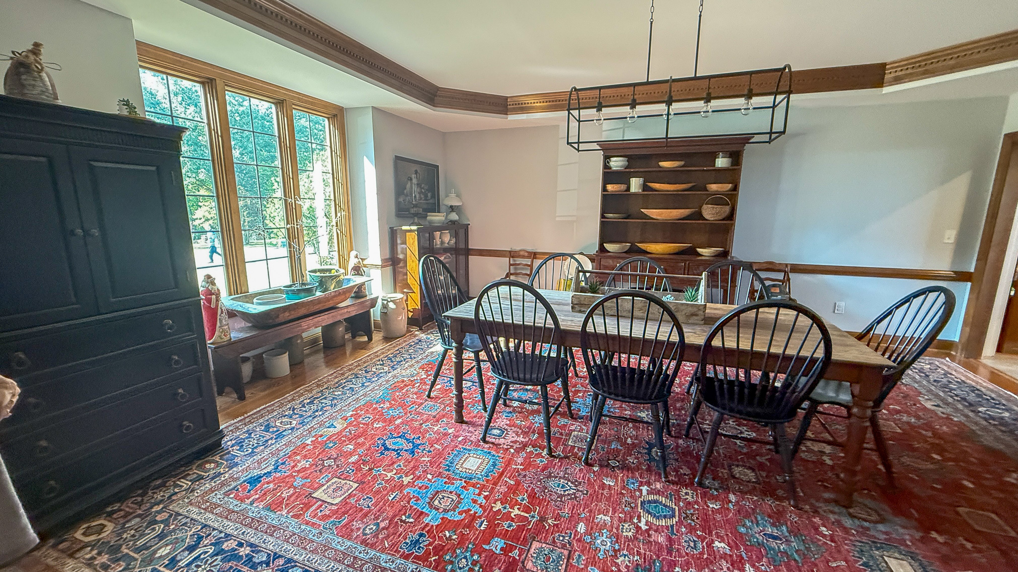 Dining room with long wooden table, black spindle chairs, patterned rug, and built-in shelves with dishware inside the home of Group home providers Rhonda and Bruce Norconk in Lynchburg, VA.