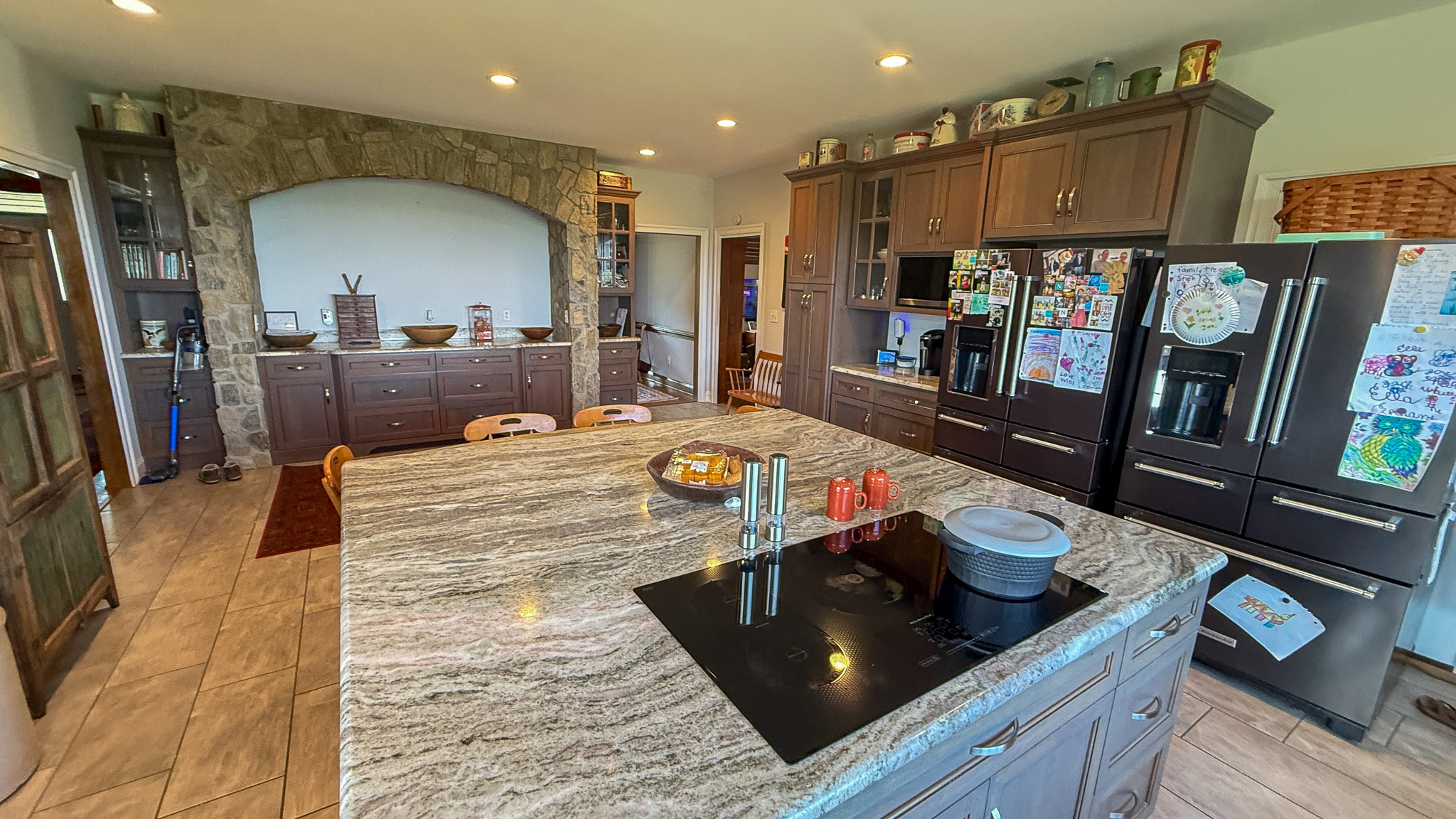 Kitchen with large island, dark cabinetry, stainless appliances, and a stone arch feature wall inside the home of Group home providers Rhonda and Bruce Norconk in Lynchburg, VA.