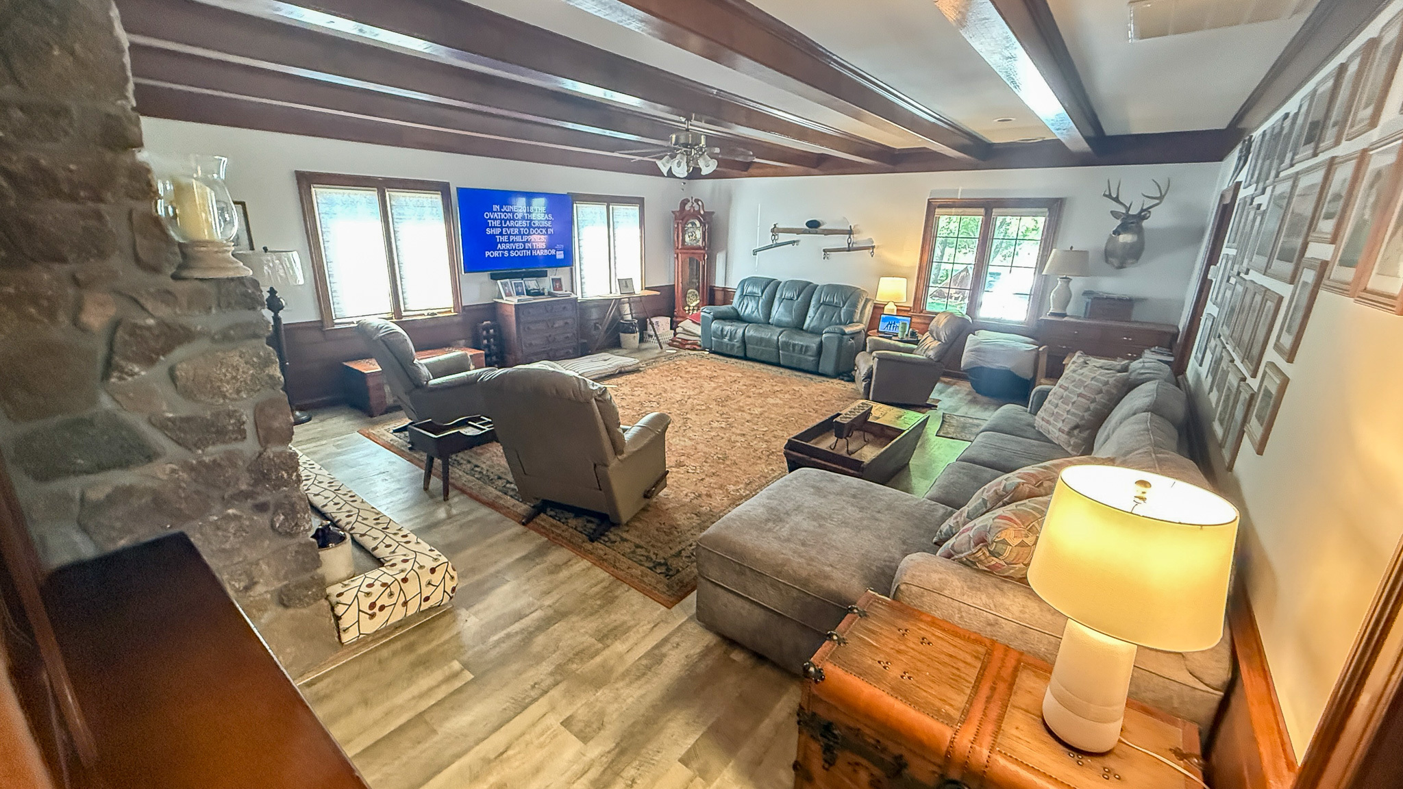 Living room with exposed wood beams, multiple seating areas, and a TV mounted above a dresser  inside the home of Group home providers Rhonda and Bruce Norconk in Lynchburg, VA.