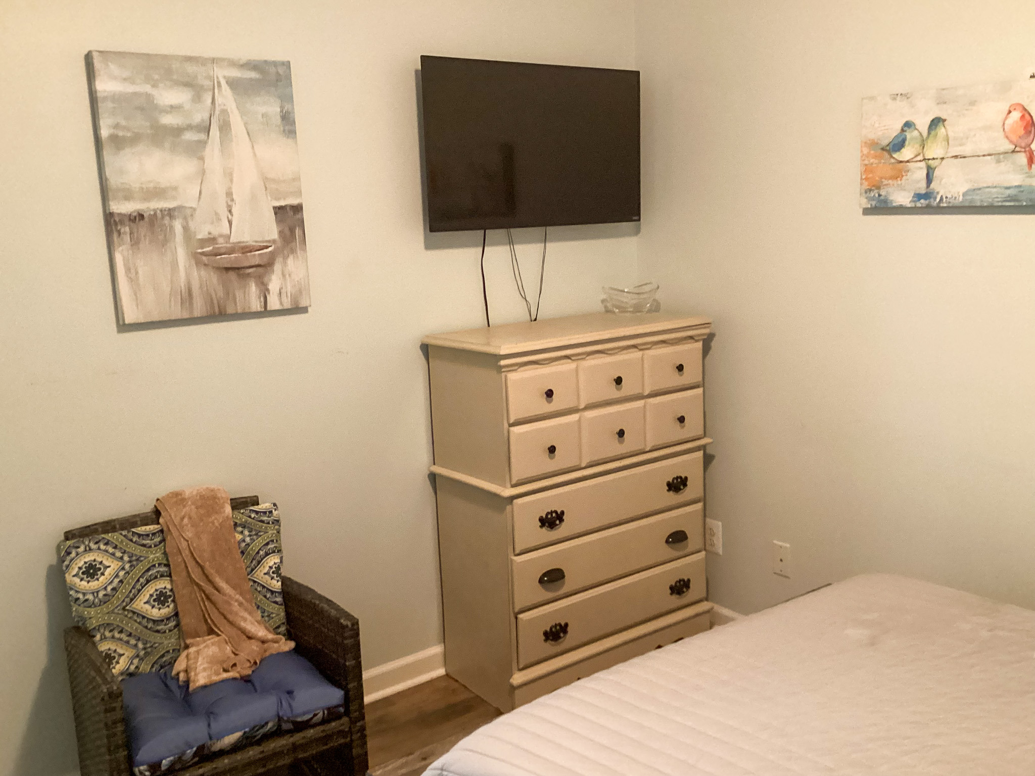 Warm, comfortable bedroom with a neatly made bed, wooden dresser with TV, andattractive decor in home of Sponsored Residential Provider Roxane Barnes.