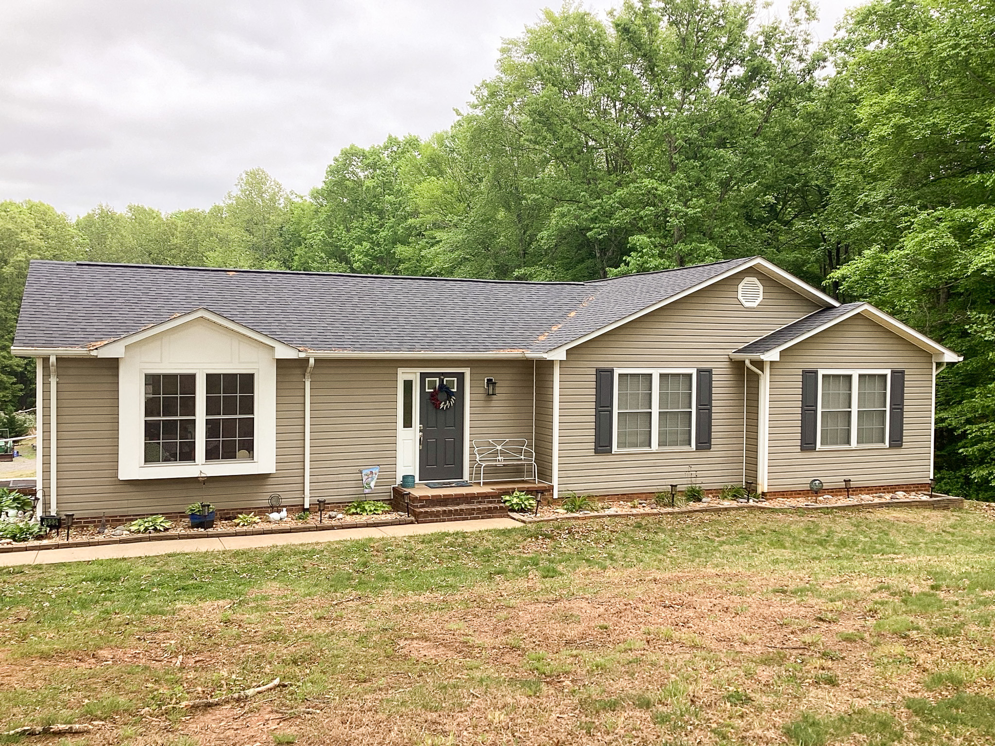 Welcoming single-story beige home with a small front porch and trees visible in the yard behind the home belonging to Sponsored Residential Provider Roxane Barnes.