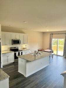 Bright kitchen with white cabinets, stainless steel appliances, and a large island, opening into a dining area with sliding glass doors inside the home of Sponsored Residential Providers Shannon and Rebeka Knott in Staunton, Virginia.