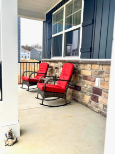 Front porch with two red cushioned rocking chairs positioned against a stone accent wall beneath a large window outside the home of Sponsored Residential Providers Shannon and Rebeka Knott in Staunton, Virginia.
