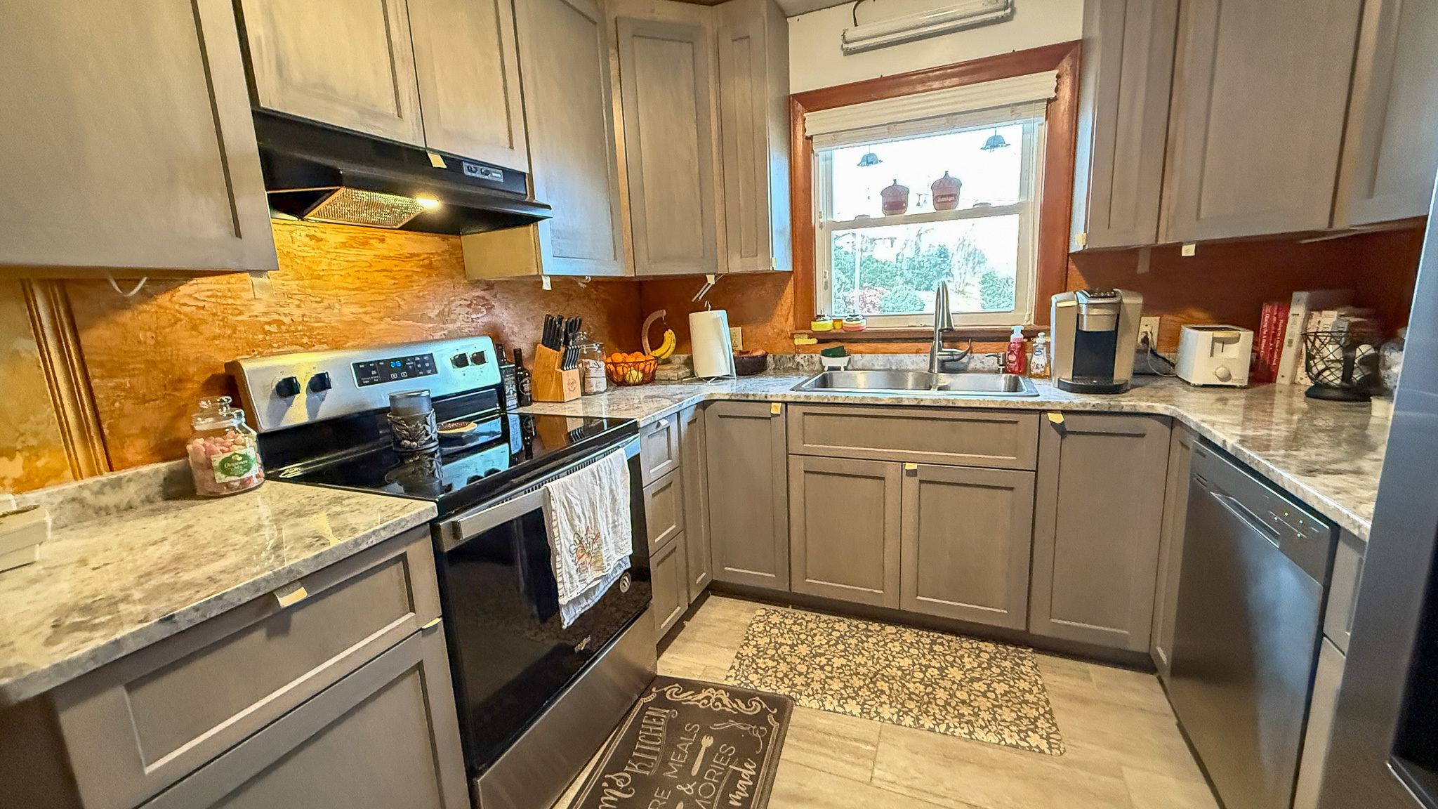 A kitchen with gray cabinetry, a stainless steel stove, and marble‑style counters surrounding a window over the sink inside the home of Sponsored Residential Providers Angela and James Snyder in Rocky Mount, Virginia.