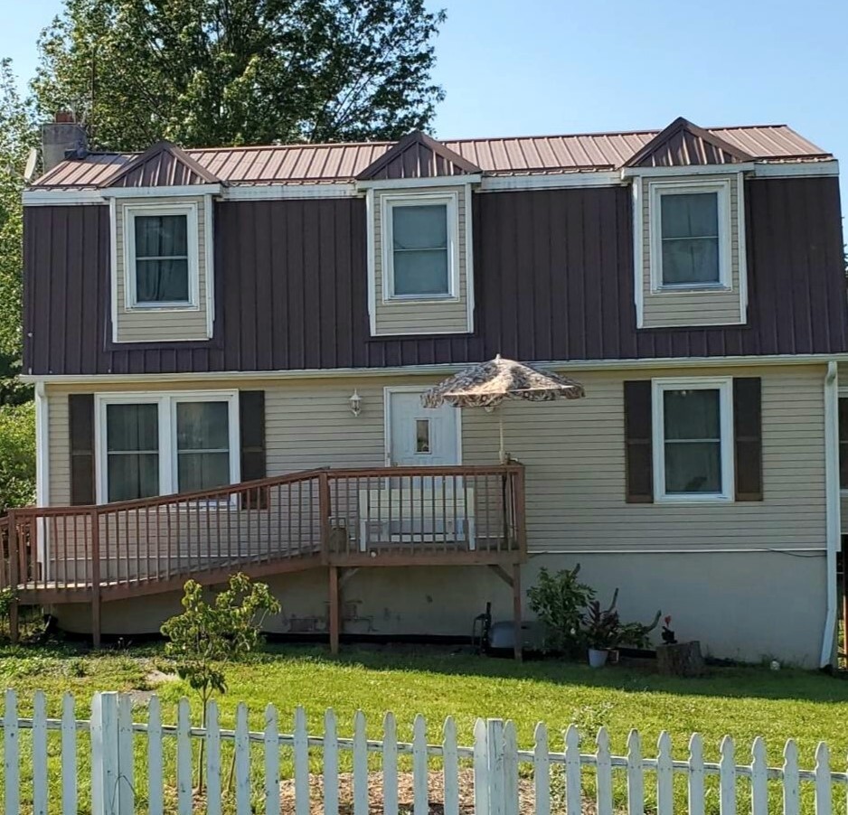 Two‑story house with tan siding, dark brown upper level, dormer windows, and a wooden accessibility ramp, behind a white picket fence belonging to Group Home Provider Tammie Atwell in Radford, Virginia.