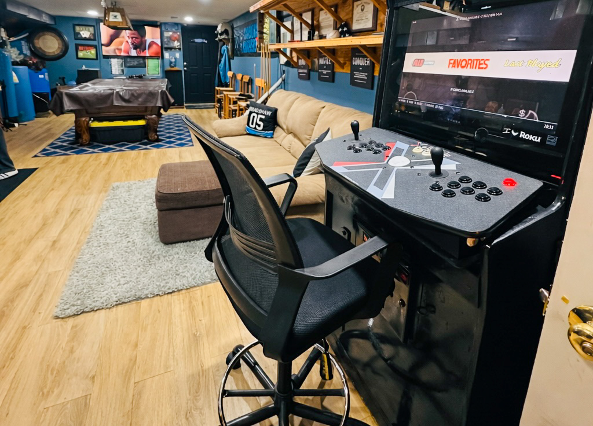 Game room with a retro arcade cabinet and chair in the foreground, with a pool table and lounge area in the background inside the home of Sponsored Residential Provider Tarnisha Bradshaw in Fredericksburg, Virginia.