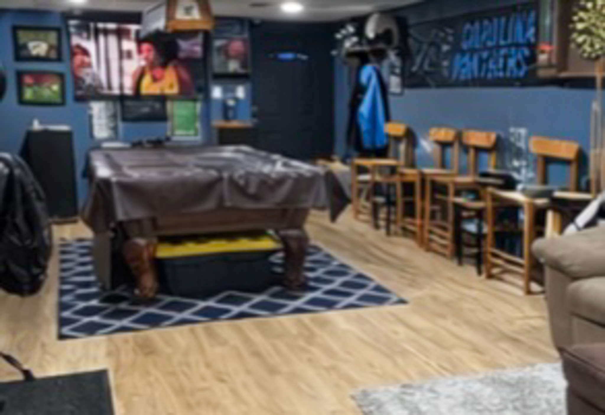 Basement game room with a covered pool table, bar stools, wall décor, and a TV playing a show inside the home of Sponsored Residential Provider Tarnisha Bradshaw in Fredericksburg, Virginia.
