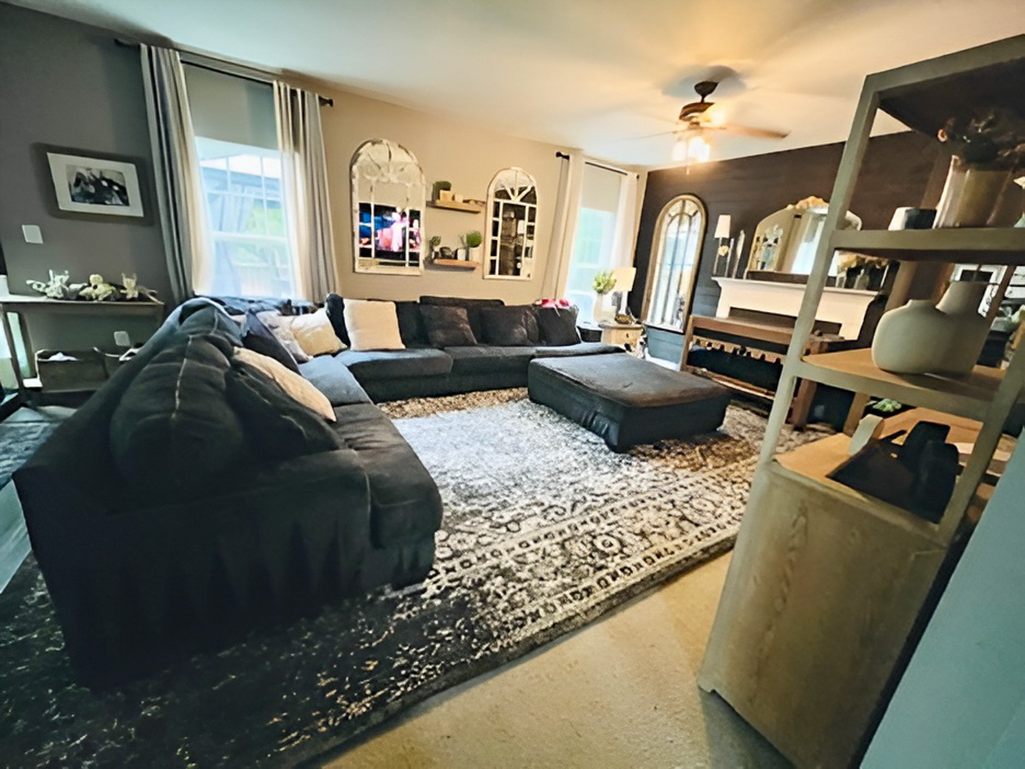 Spacious living room with a large dark sectional, patterned rug, mirrors on the wall, and multiple windows letting in natural light inside the home of Group Home Providers Alex and Dillon Tittle in Fredericksburg, Virginia.